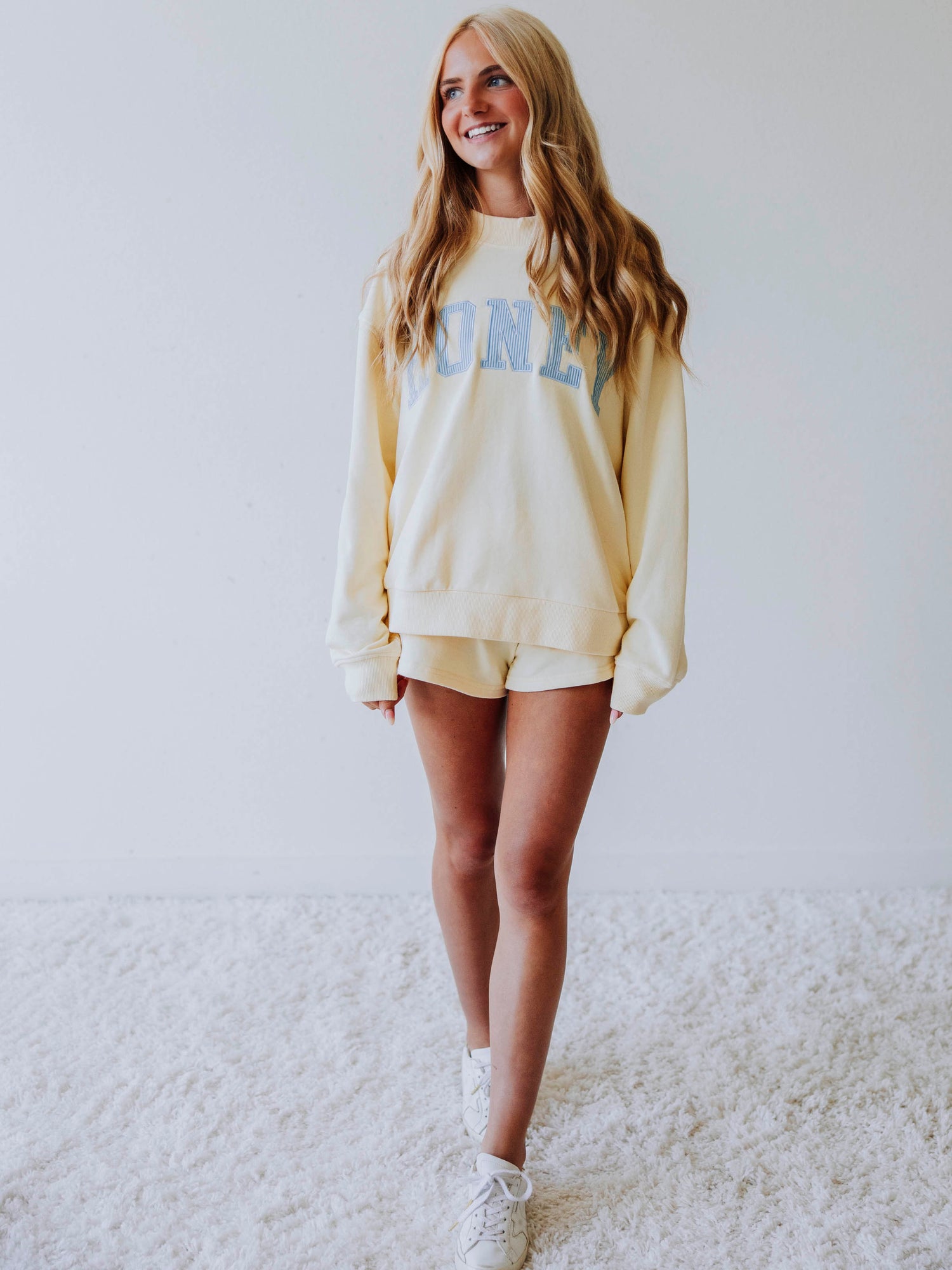 Girl wearing a soft, yellow two piece set. Top says HONEY on the front. The HONEY has blue lines going through each letter. Shorts are same yellow as top. 