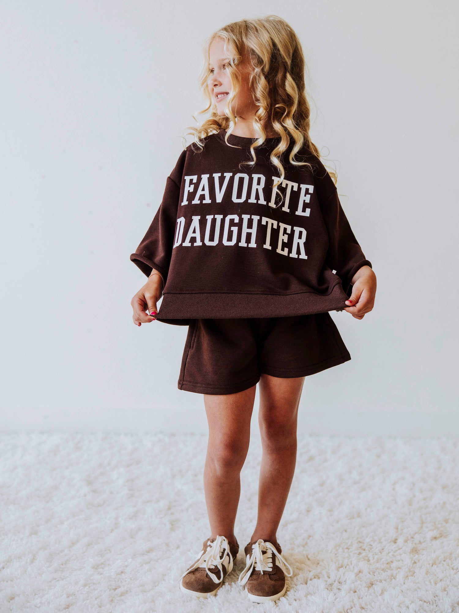 Model wearing a two piece chocolate colored jogging set. Top says FAVORITE DAIGHTER. Bell hem sleeves with chocolate colored shorts. 