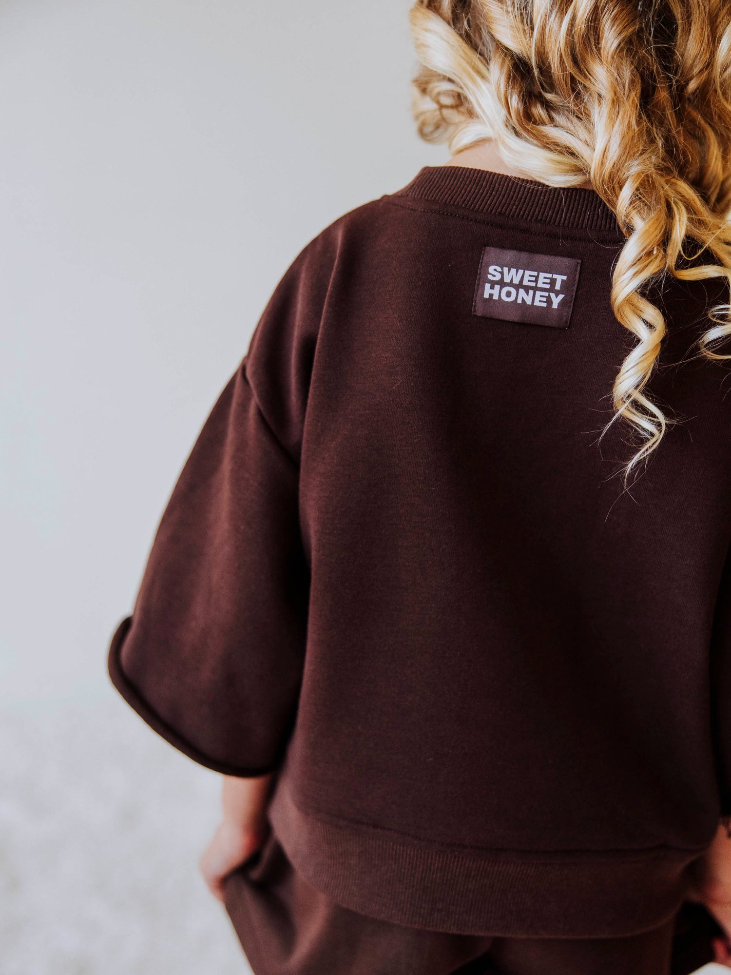 Model wearing a two piece chocolate colored jogging set. Top says FAVORITE DAIGHTER. Bell hem sleeves with chocolate colored shorts. Back of shirt has attached SweetHoney tag. 