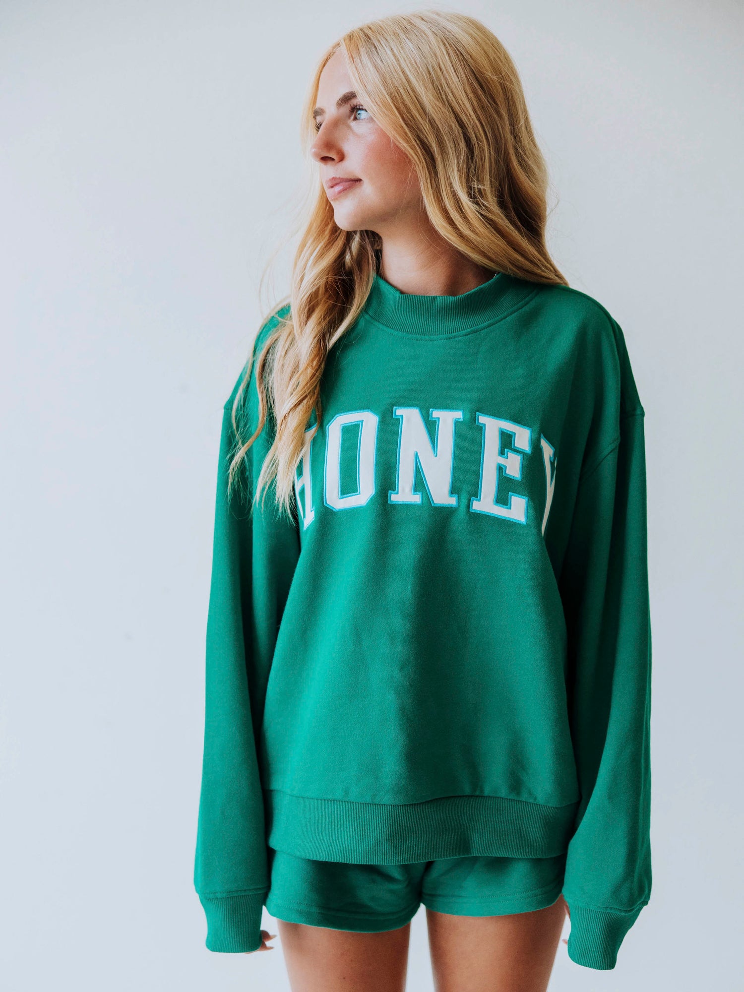 Girl wearing a teal two piece set. Top says HONEY on the front. Shorts are same teal color as top. 