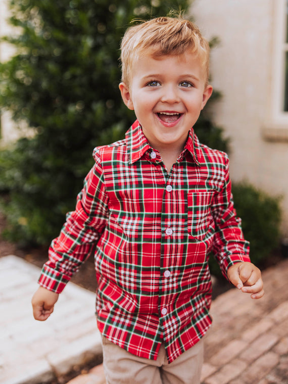 Boy outside smiling wearing a traditional red Christmas plaid button up shirt. 