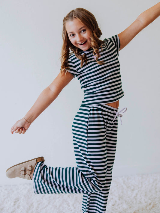 Girl is wearing a two piece, green and gray striped pant set. Model is wearing clog shoes and is posing. 