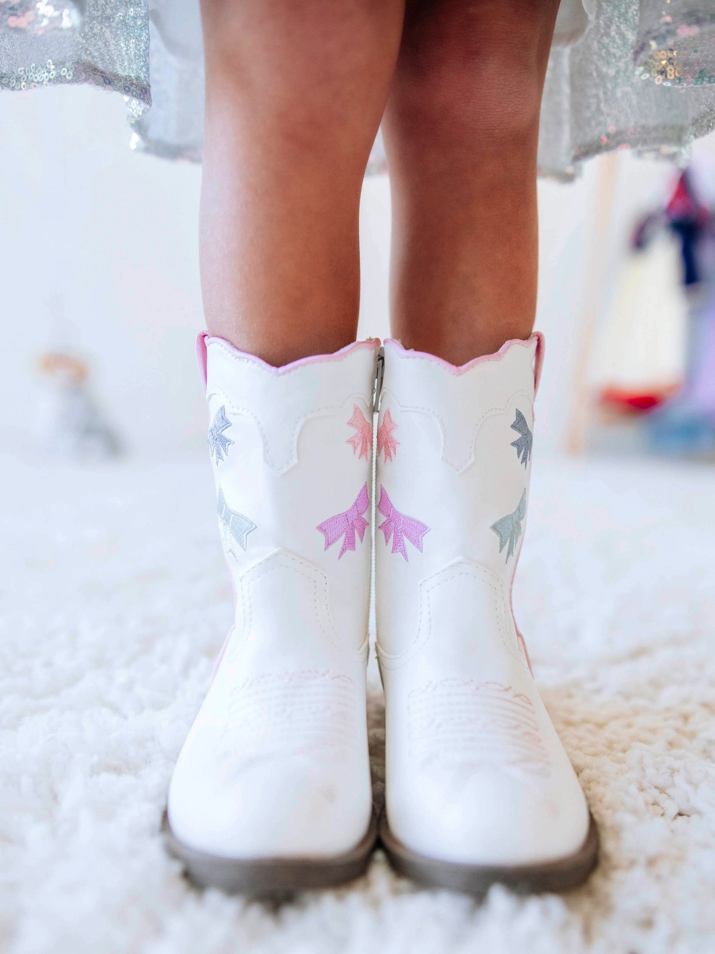 Step into sweetness with our Girls Bow Paneled Cowboy Boots, designed for twirls, giggles, and all-day play. These white faux-leather boots feature pastel pink, blue, and lavender star embroidery, charming bow panels, and an easy side zipper closure for quick on-and-off. With a soft interior lining and sturdy sole, these girls’ Western boots perfectly blend comfort and style—ideal for everyday wear, special occasions, or matching with her favorite SweetHoney dress.