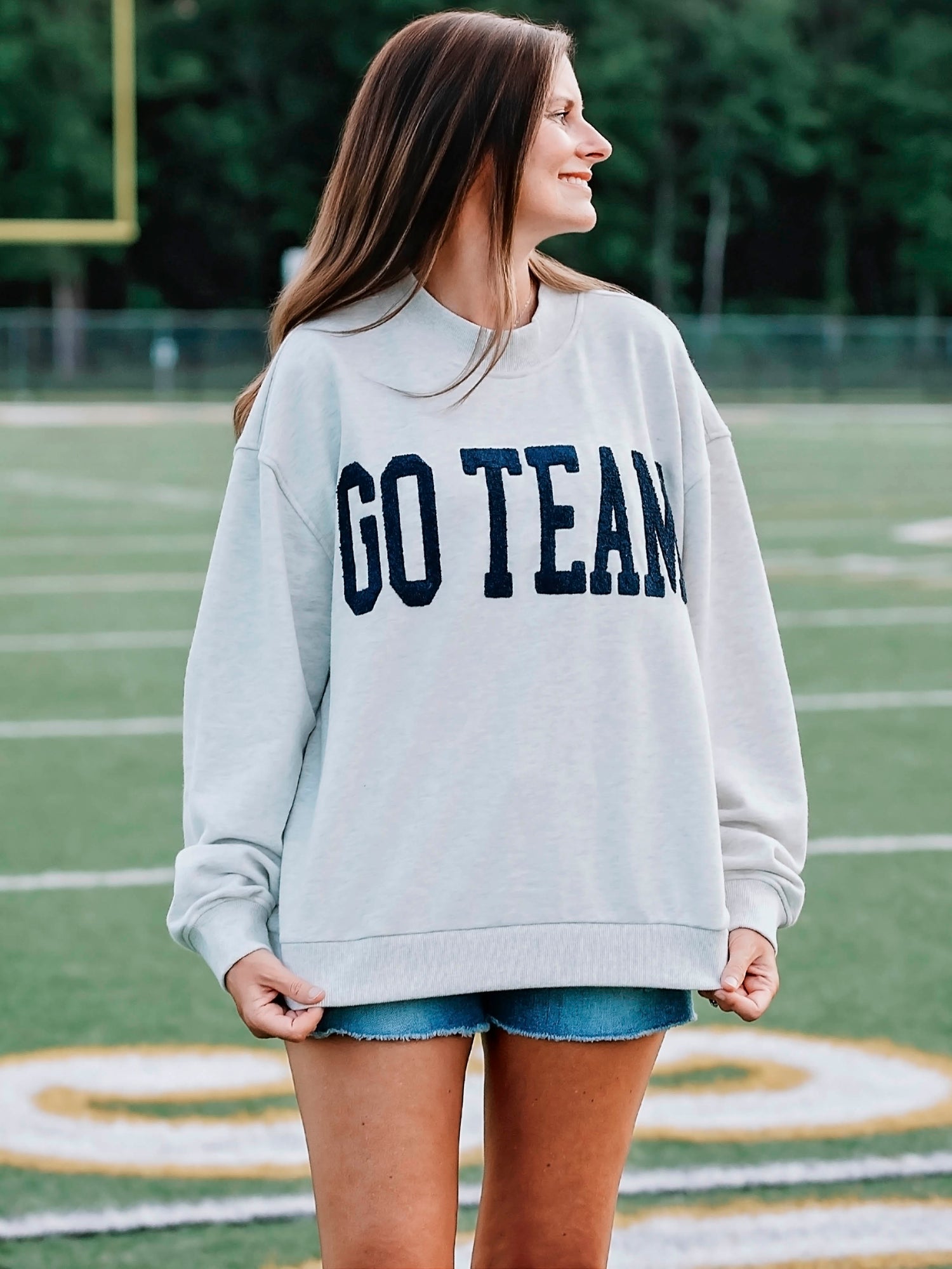 Women outside wearing a heathered gray sweater that says GO TEAM in a deep navy color