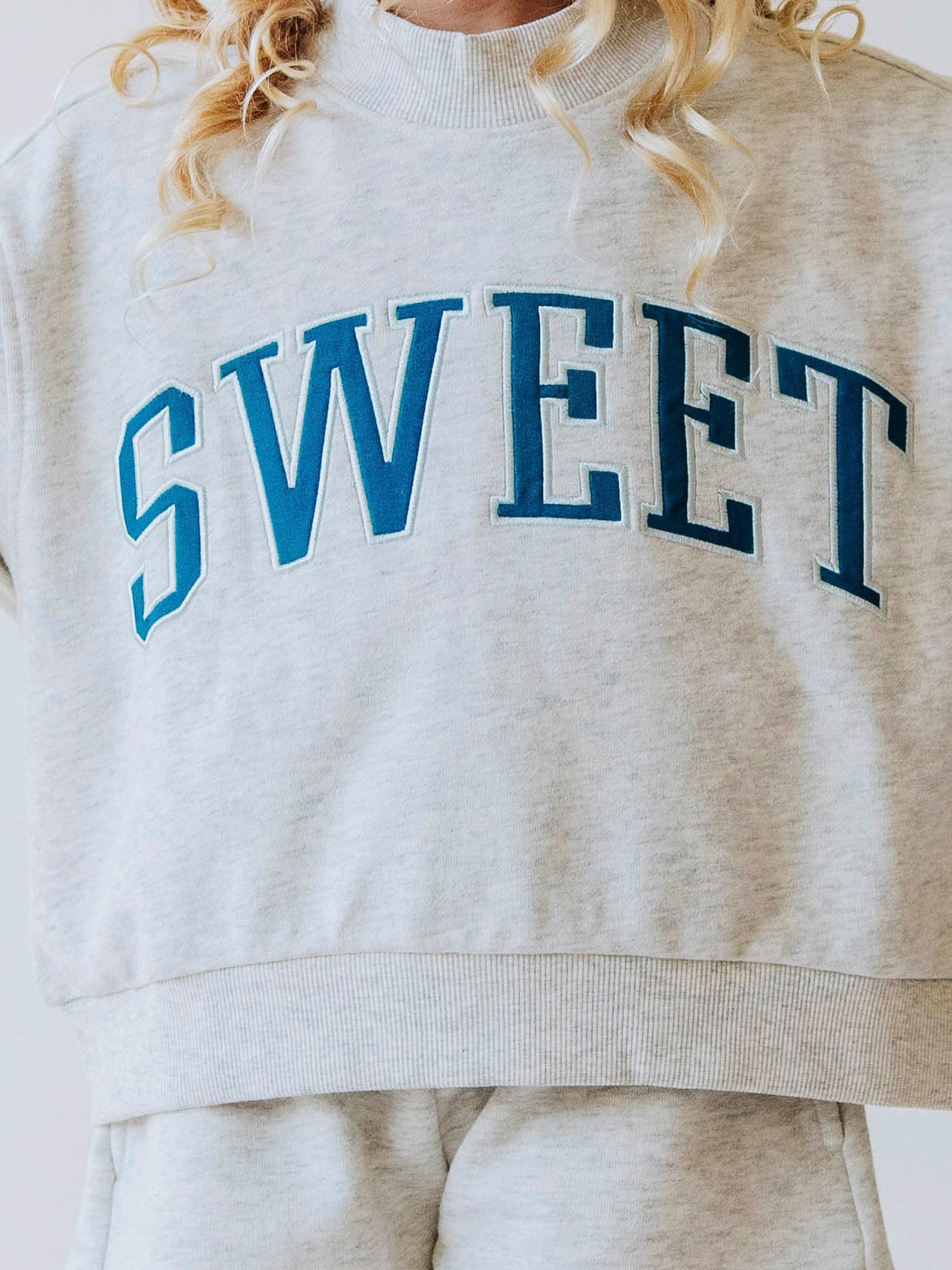 Girl model wearing a two piece gray in color set. The top says SWEET on the front in blue letters. 