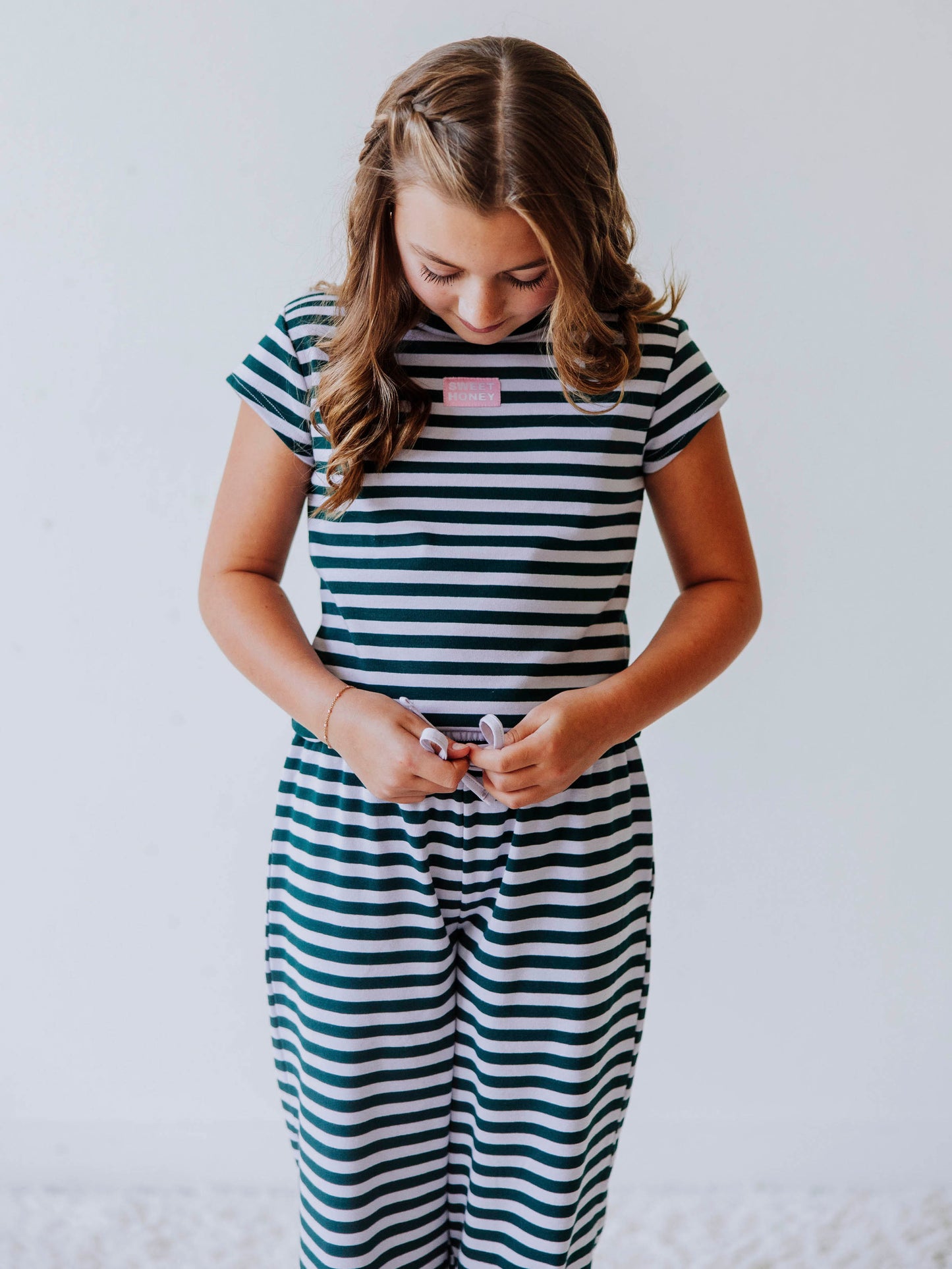 Girl is wearing a two piece, green and gray striped pant set. Top has a pink and white SweetHoney tag centered in the middle of chest. 