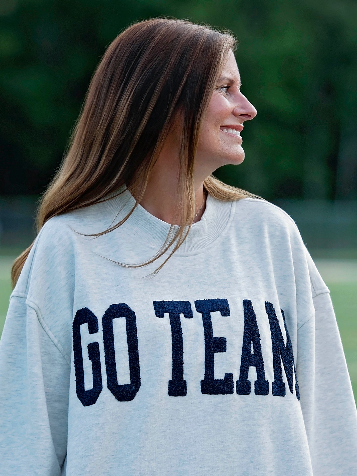 Women outside wearing a heathered gray sweater that says GO TEAM in a deep navy color