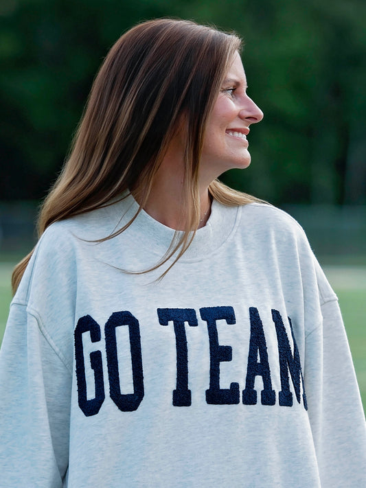 Women outside wearing a heathered gray sweater that says GO TEAM in a deep navy color