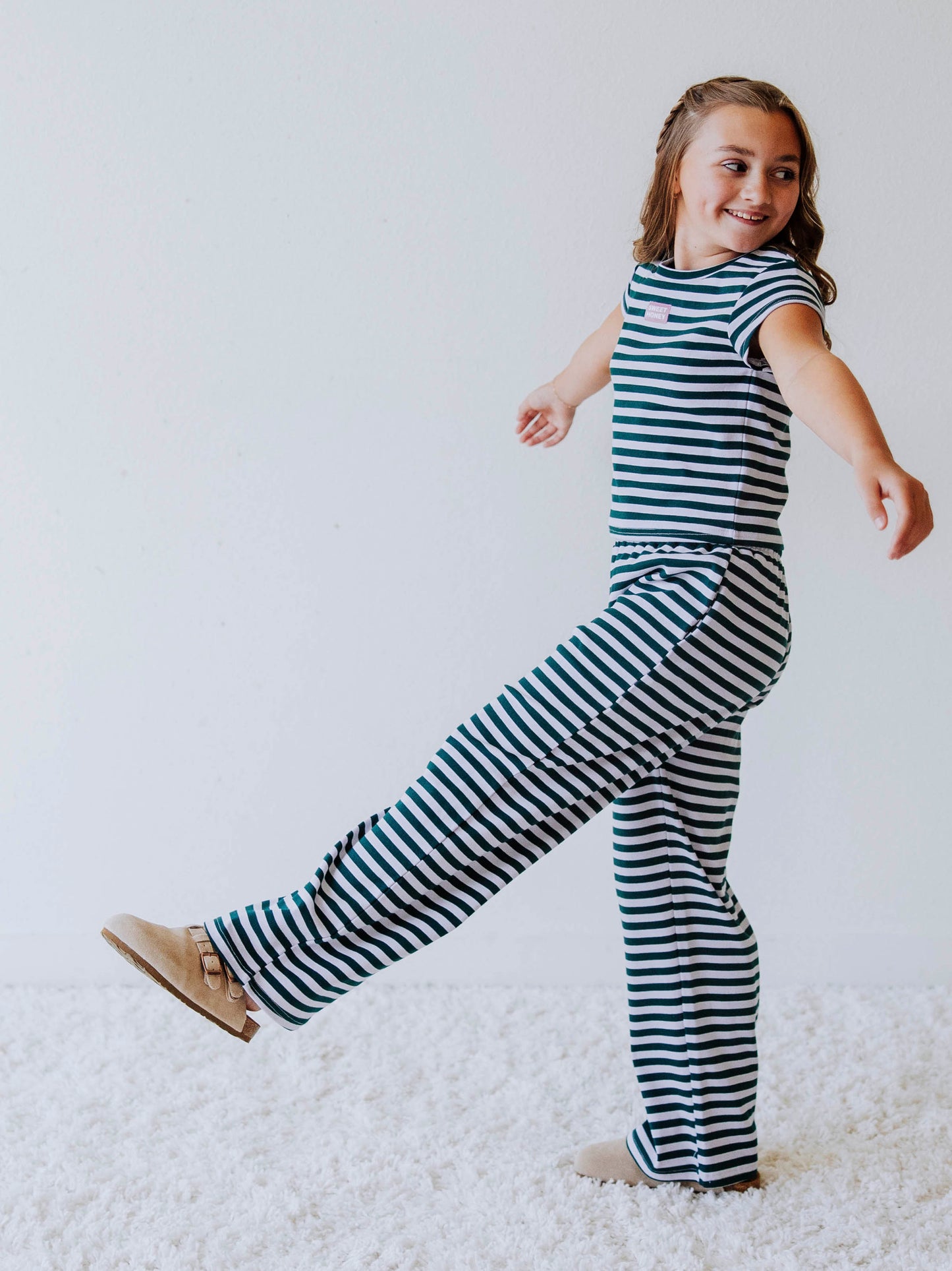 Girl is wearing a two piece, green and gray striped pant set. Model is wearing clog shoes and is posing. 