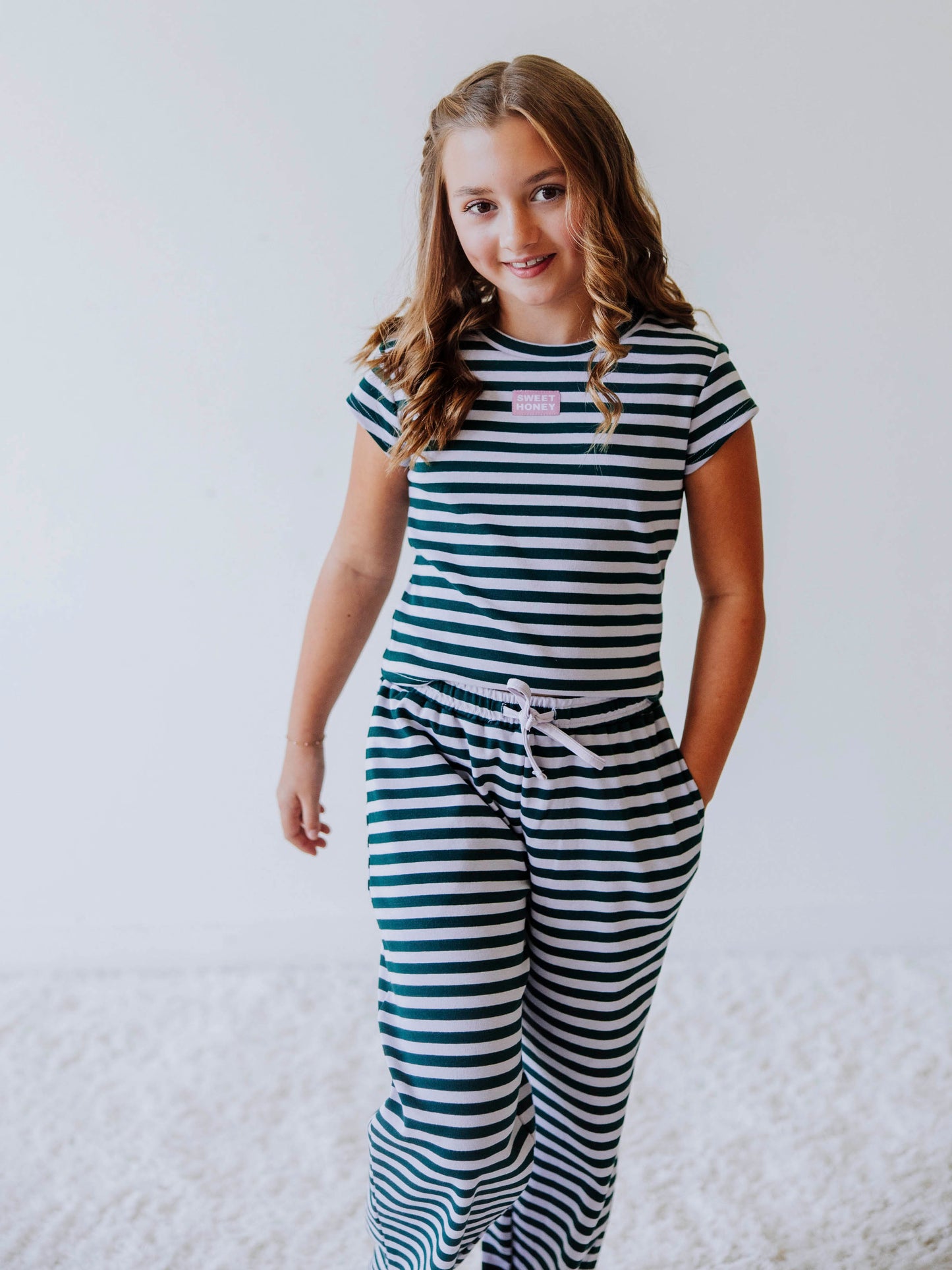 Girl is wearing a two piece, green and gray striped pant set and has hand in pocket