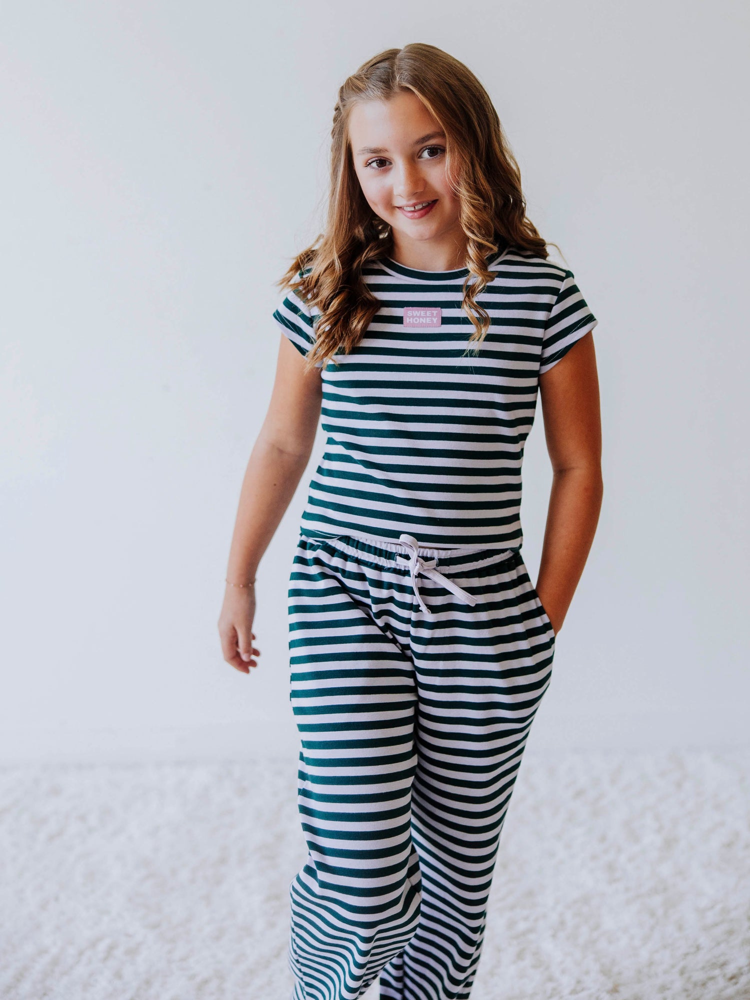Girl is wearing a two piece, green and gray striped pant set and has hand in pocket