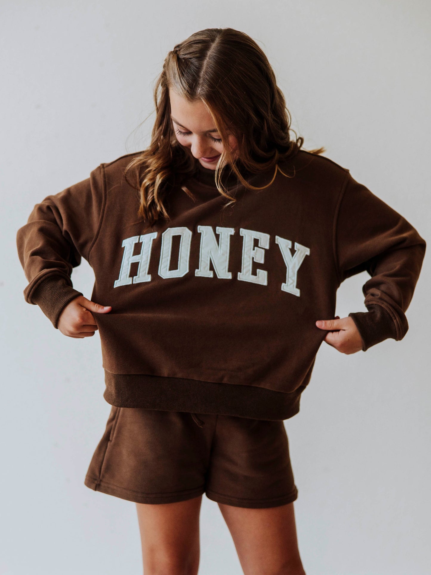 Model is wearing a two-piece, brown colored mock neck style set. Top has HONEY across the top in ivory colored letters. Bottoms are the same color as top. 