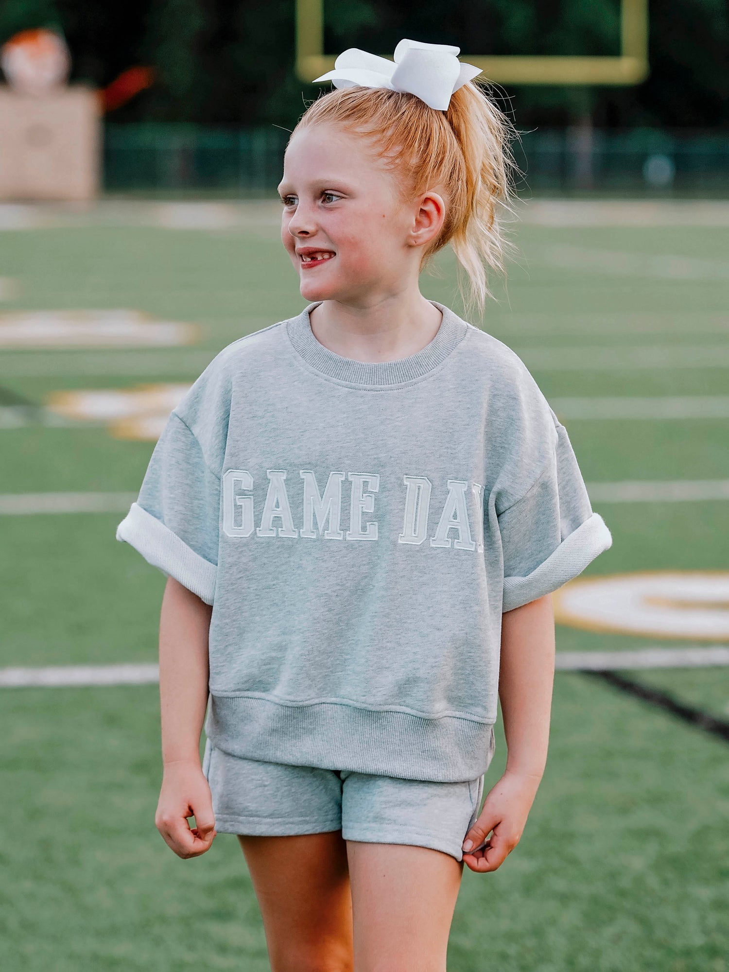 Girl outside wearing a two-piece gray sweat set that says GAME DAY on the front. 