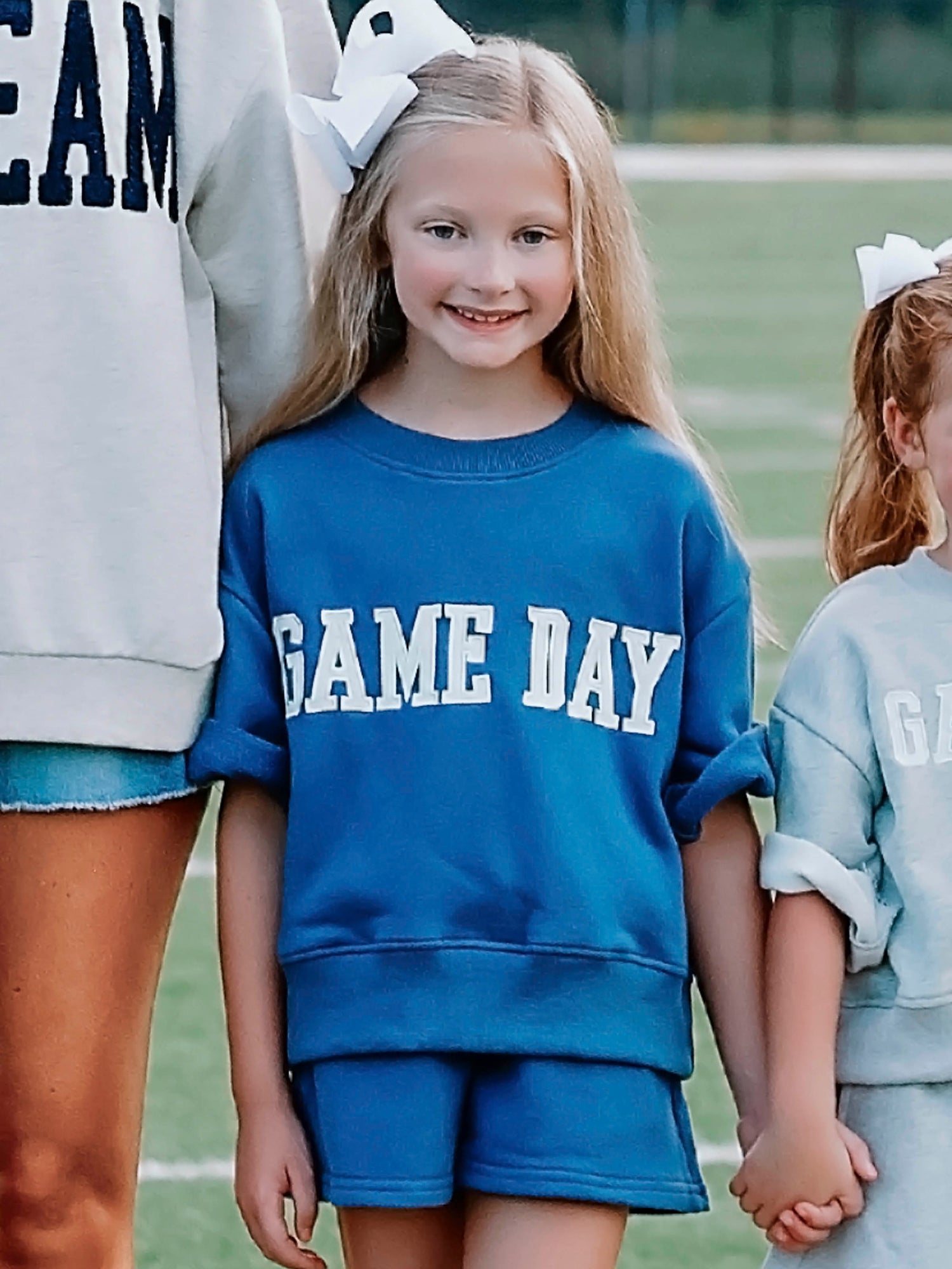 Girl outside wearing a two piece navy set that says GAME DAY on the front. Girl is holding hands with others. 