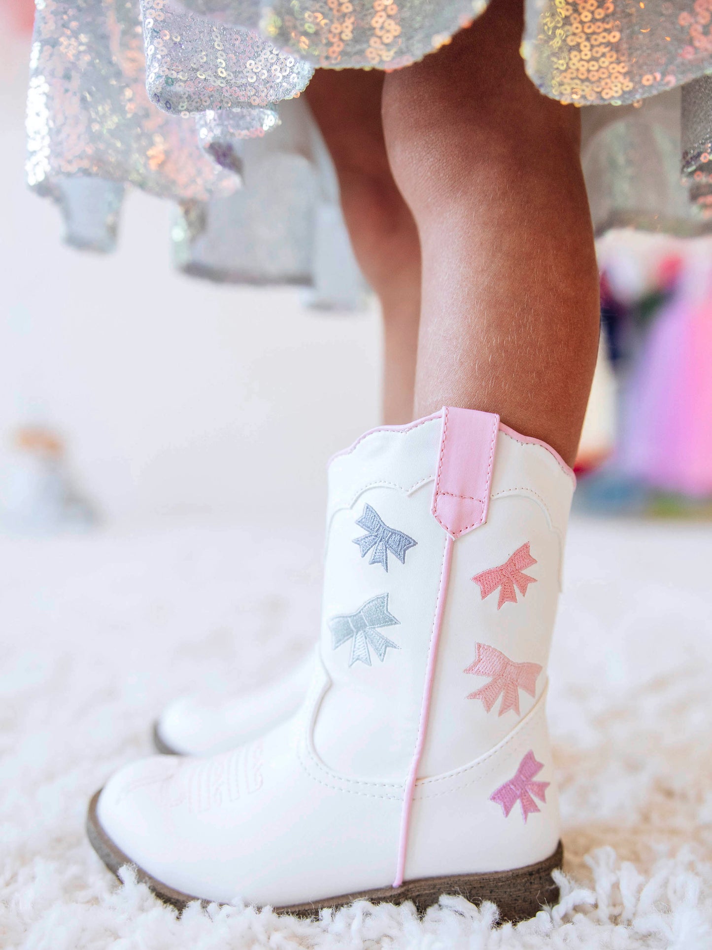Step into sweetness with our Girls Bow Paneled Cowboy Boots, designed for twirls, giggles, and all-day play. These white faux-leather boots feature pastel pink, blue, and lavender star embroidery, charming bow panels, and an easy side zipper closure for quick on-and-off. With a soft interior lining and sturdy sole, these girls’ Western boots perfectly blend comfort and style—ideal for everyday wear, special occasions, or matching with her favorite SweetHoney dress.