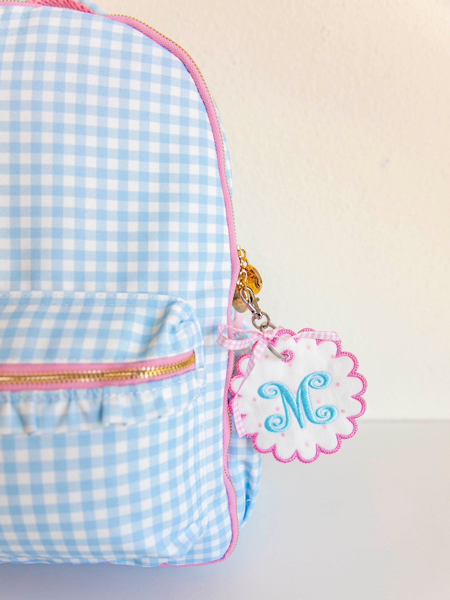 Blue gingham backpack with a customized tag hanging off a zipper. 