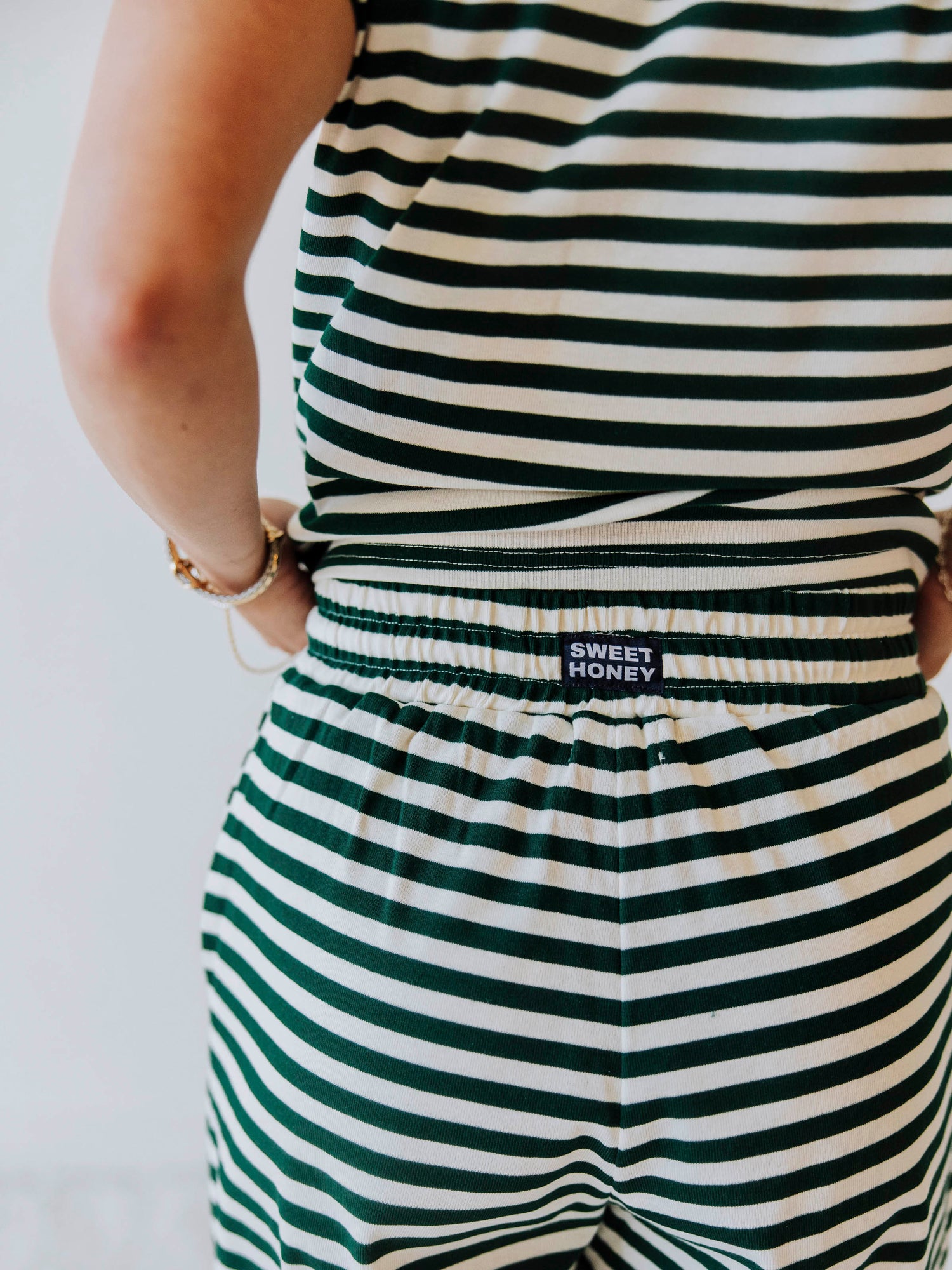 Model is in a studio and is wearing a two piece hunter green and ivory set. Shown is a close-up of the SweetHoney logo tag located on the back of the waistband.