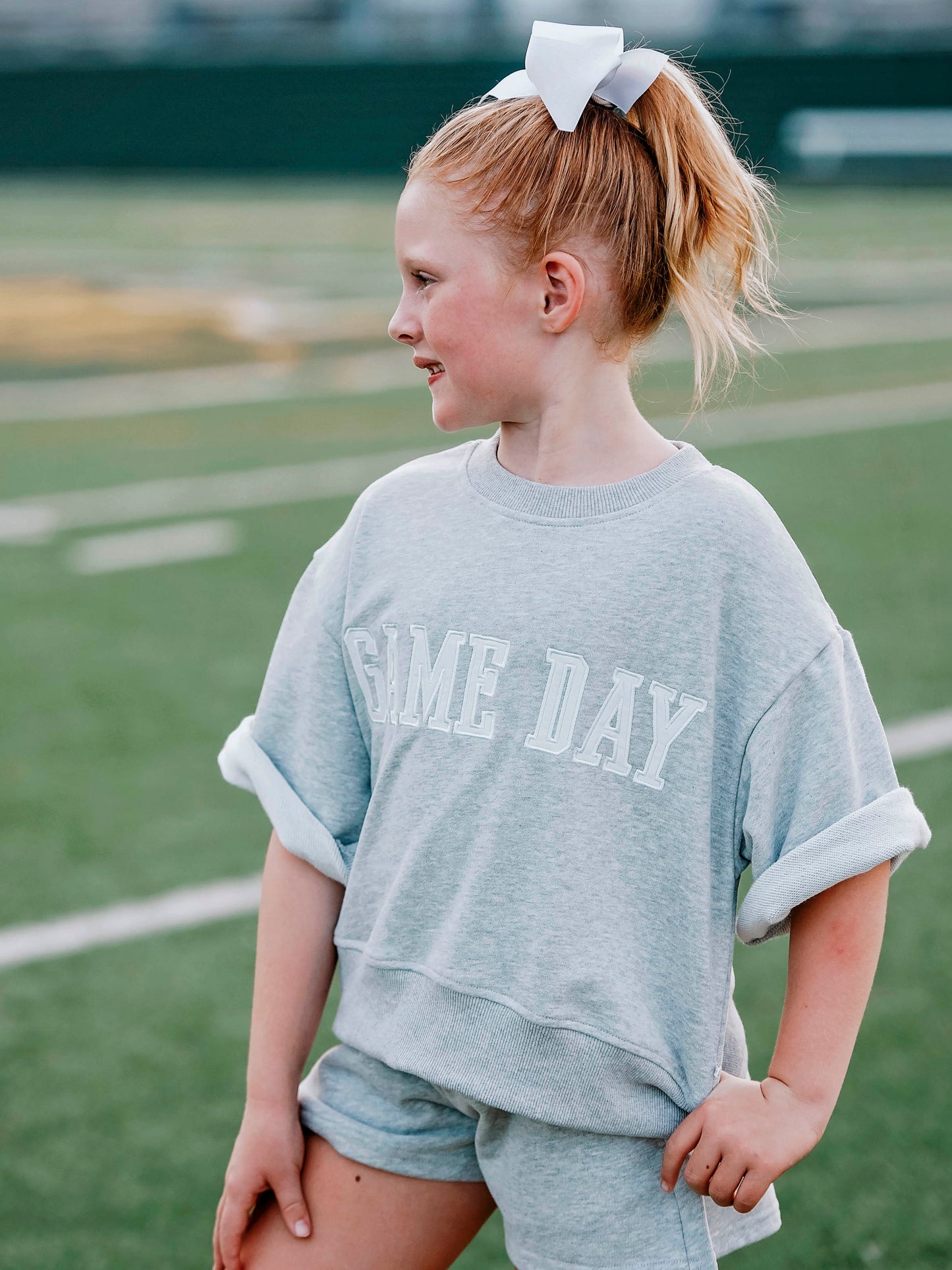 Girl outside wearing a two-piece gray sweat set that says GAME DAY on the front. 