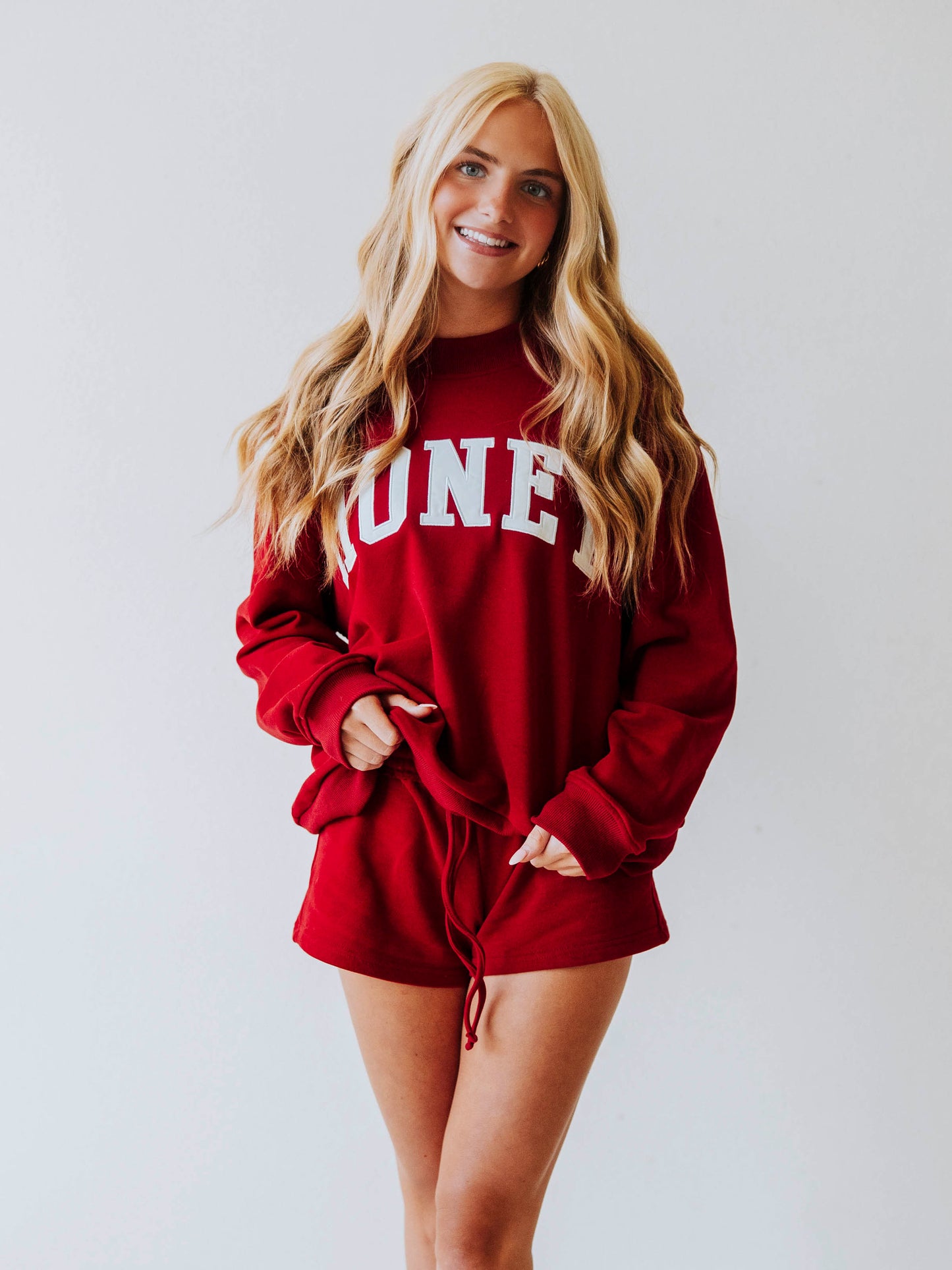 Girl wearing a two piece, crimson colored set. The top is a mock neck style that says HONEY on the front and the bottoms are plain. 