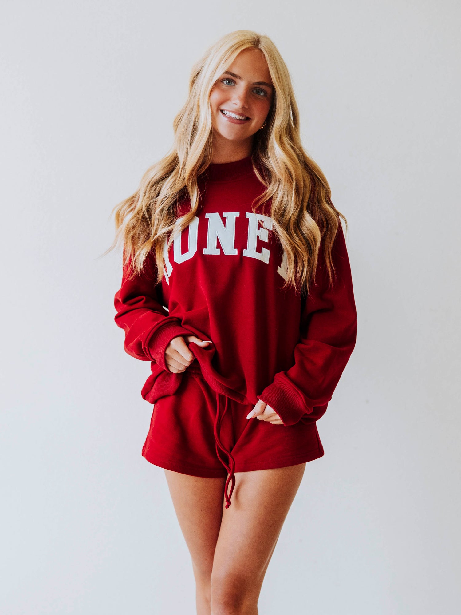 Girl wearing a two piece, crimson colored set. The top is a mock neck style that says HONEY on the front and the bottoms are plain. 
