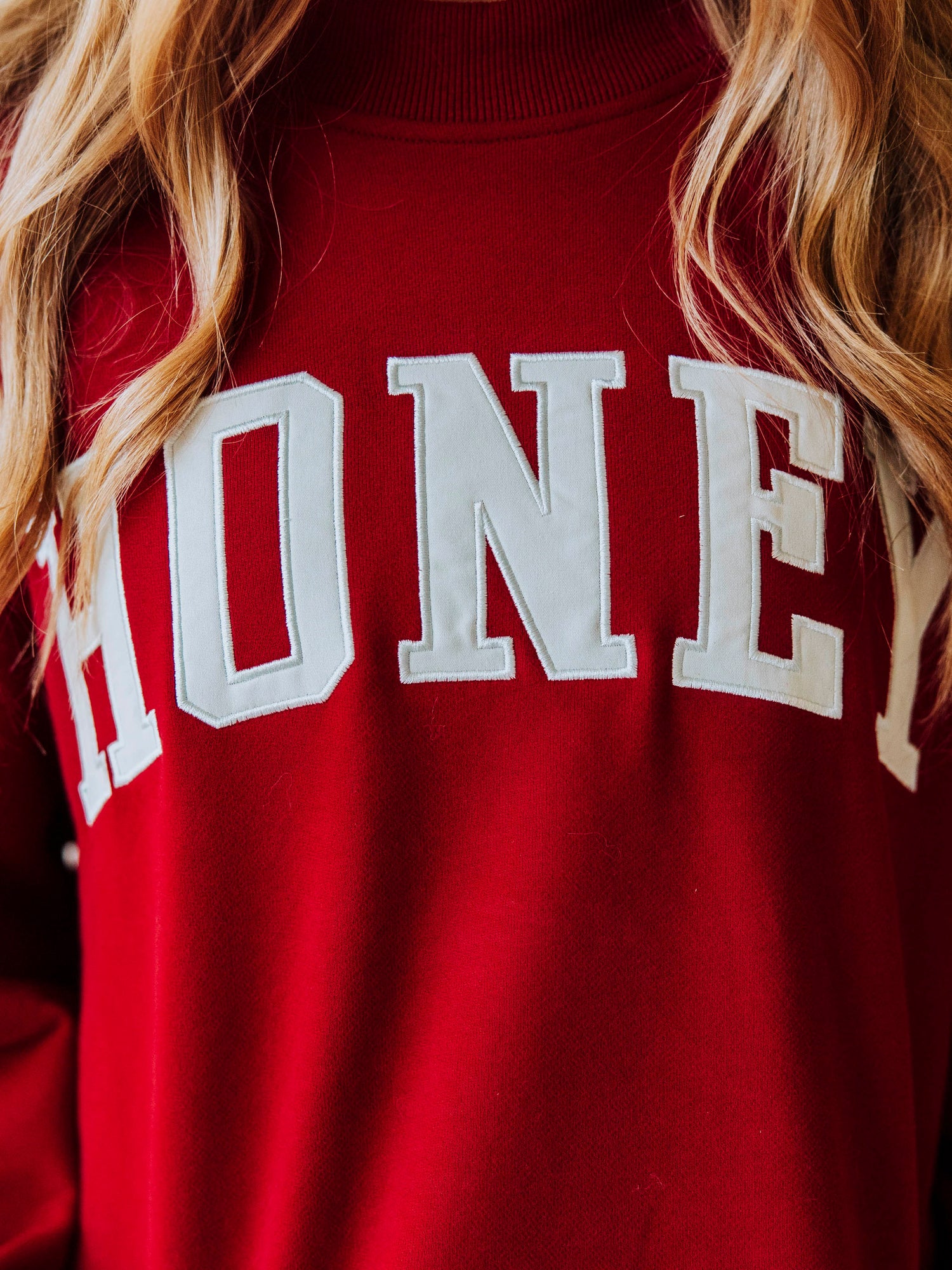 Close up of girl wearing a crimson colored sweatshirt that says HONEY on it