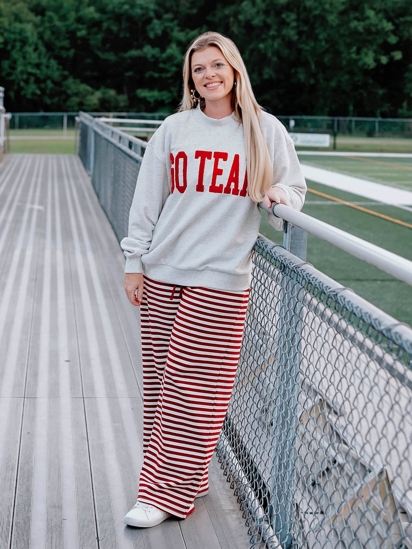Women outside wearing a heathered gray sweatshirt that says GO TEAM in a crimson red color. She is wearing crimson red striped pants