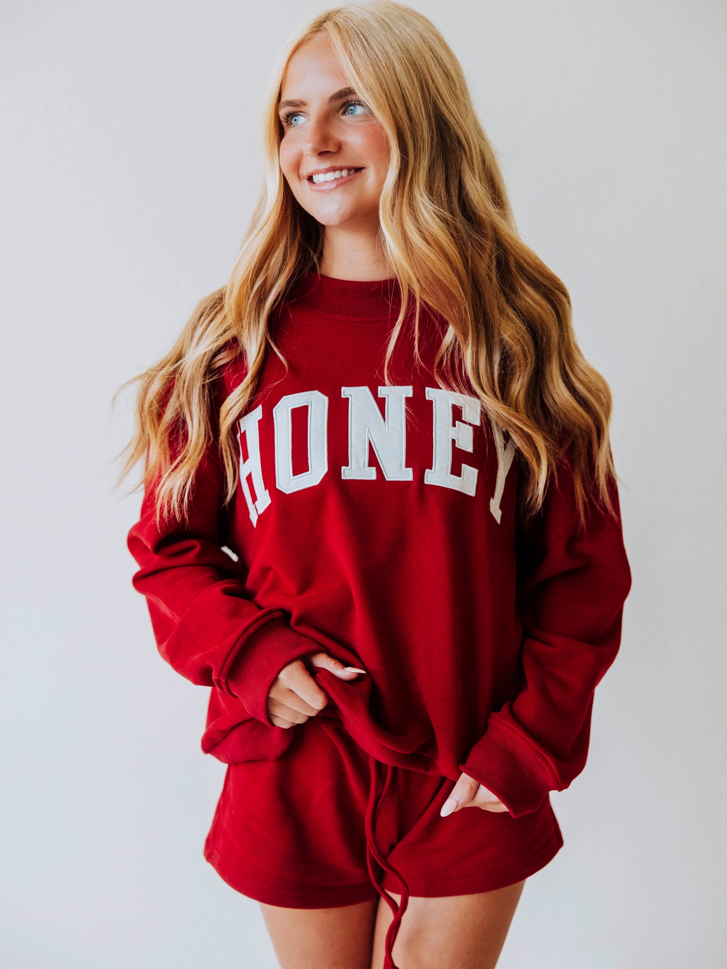 Girl wearing a two piece, crimson colored set. The top is a mock neck style that says HONEY on the front and the bottoms are plain. 