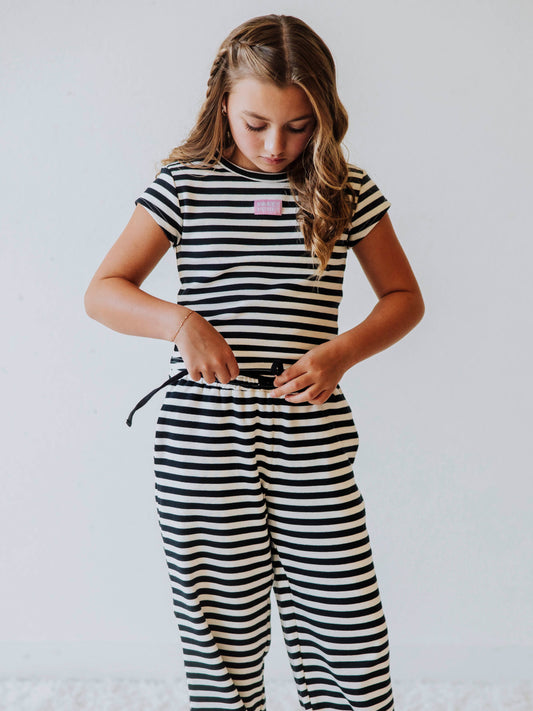 Girl is wearing a two-piece, navy and ivory striped pant set. There is a SweetHoney logo tag stitched on the center of shirt. 