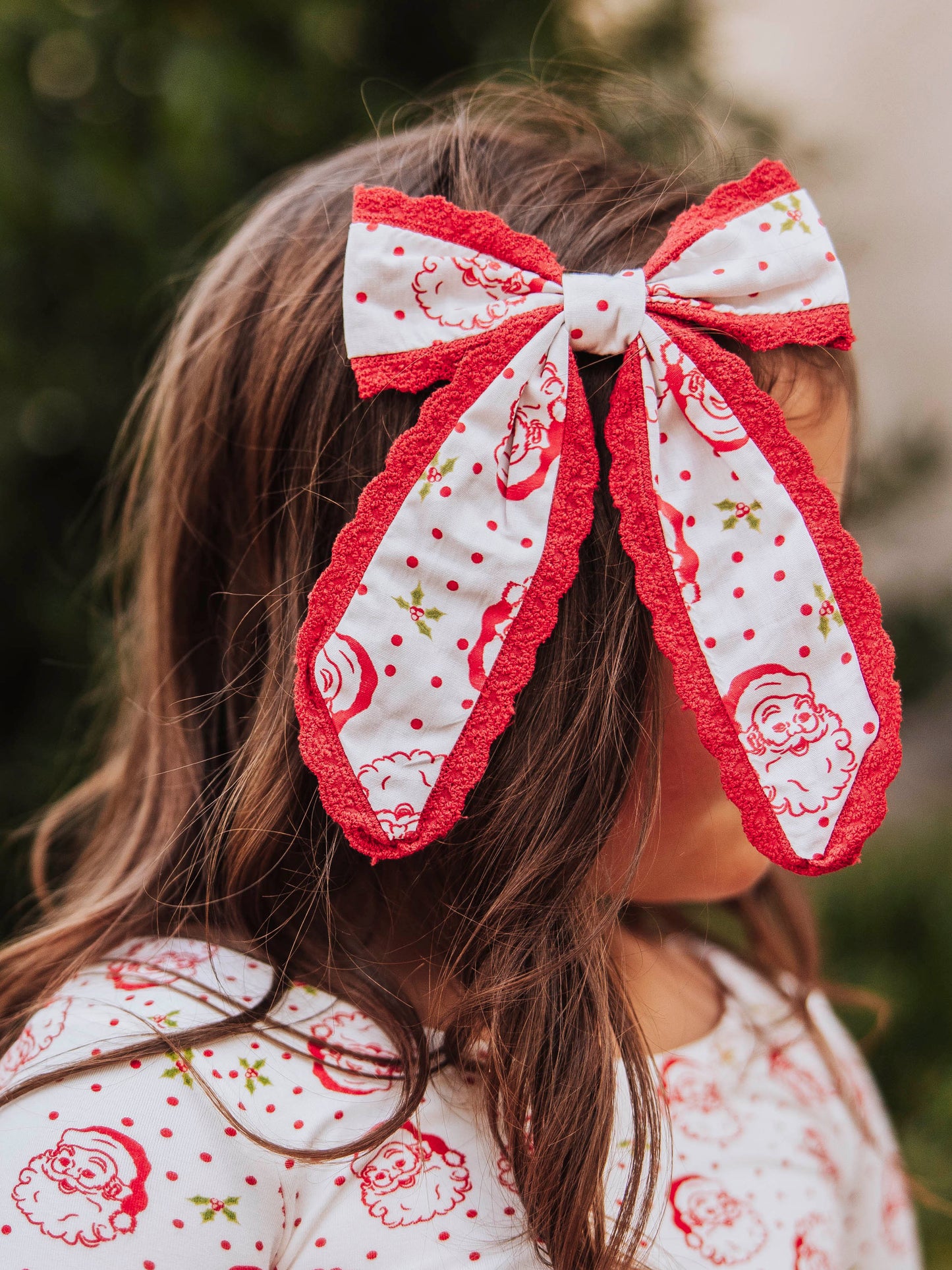Model wearing a polka dot Santa bow trimmed in red and is wearing the same printed top. 