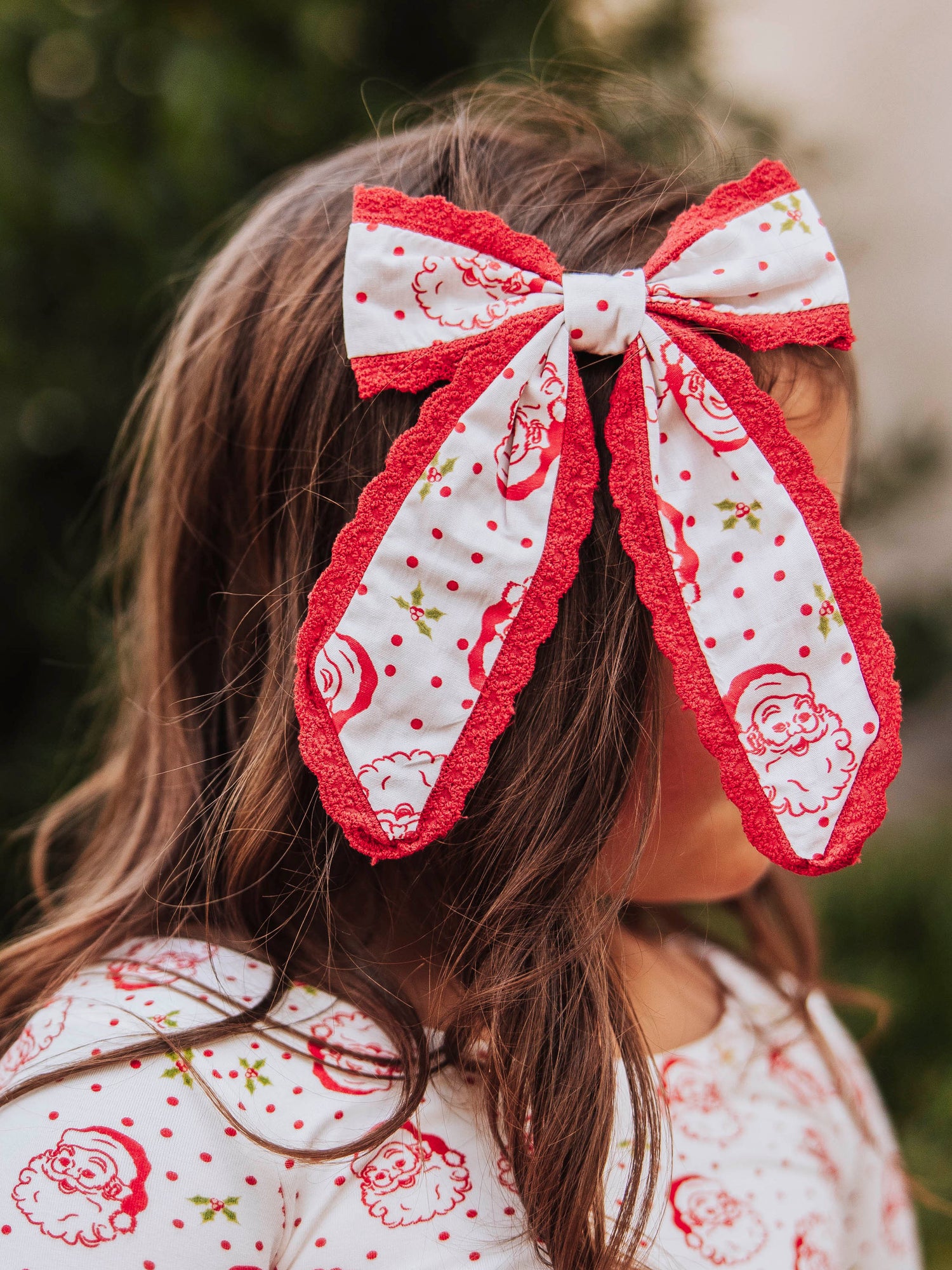 Model wearing a polka dot Santa bow trimmed in red and is wearing the same printed top. 