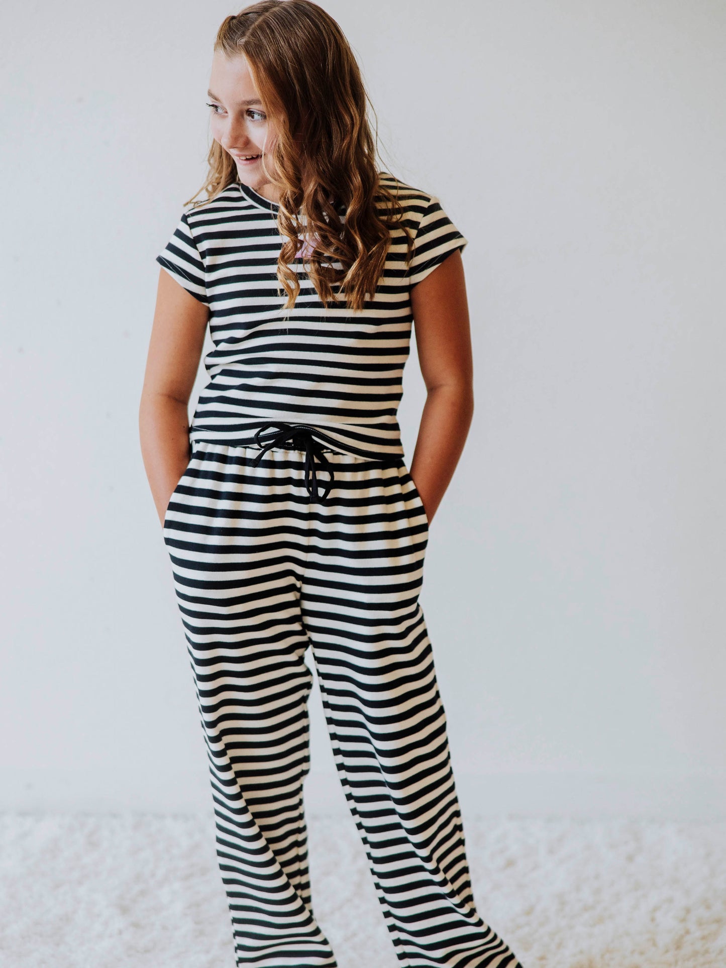 Girl is wearing a two-piece, navy and ivory striped pant set. There is a SweetHoney logo tag stitched on the center of shirt. 