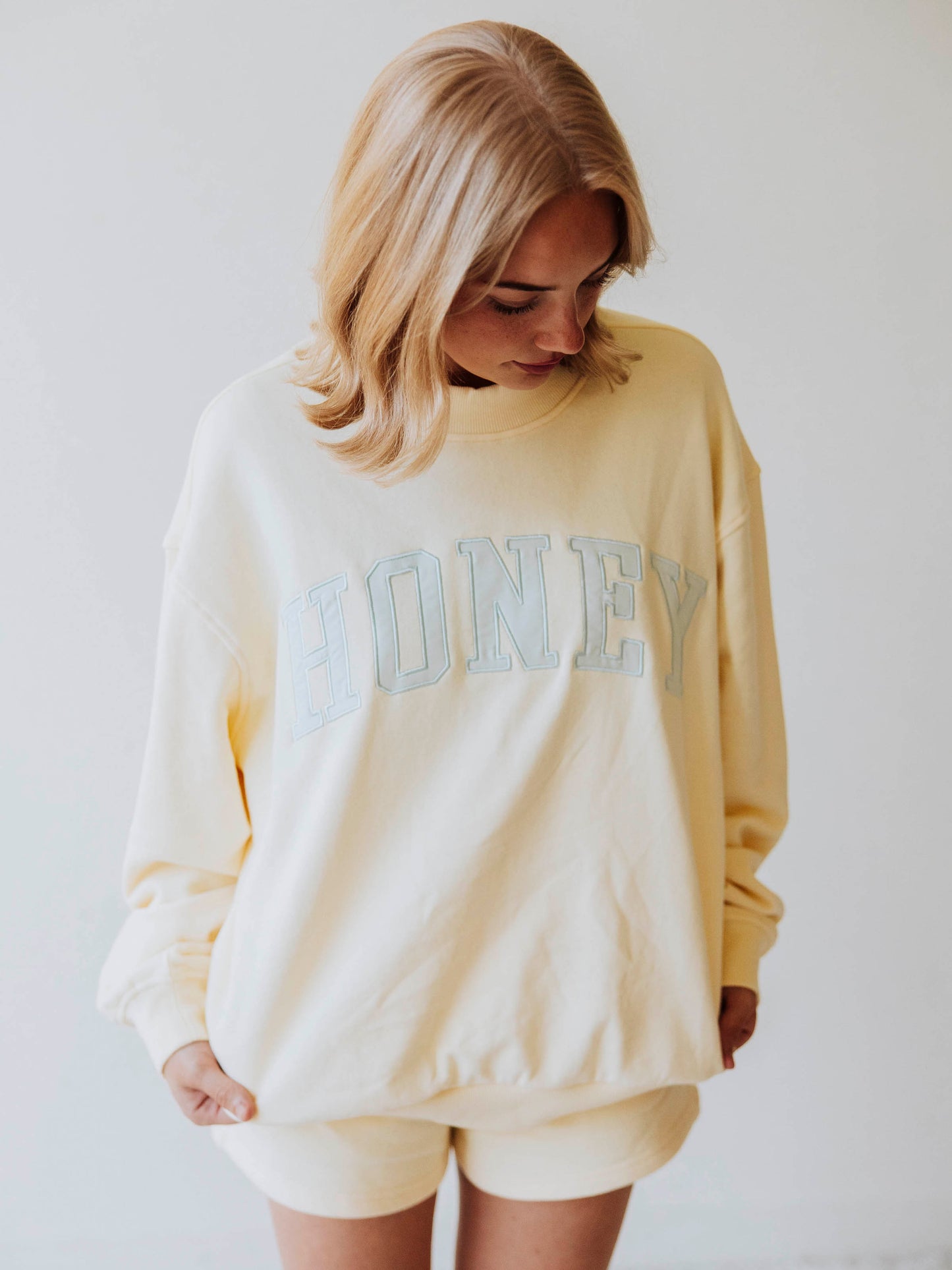 Girl wearing a two-piece soft yellow set that says HONEY on the front in a light bluish color. 