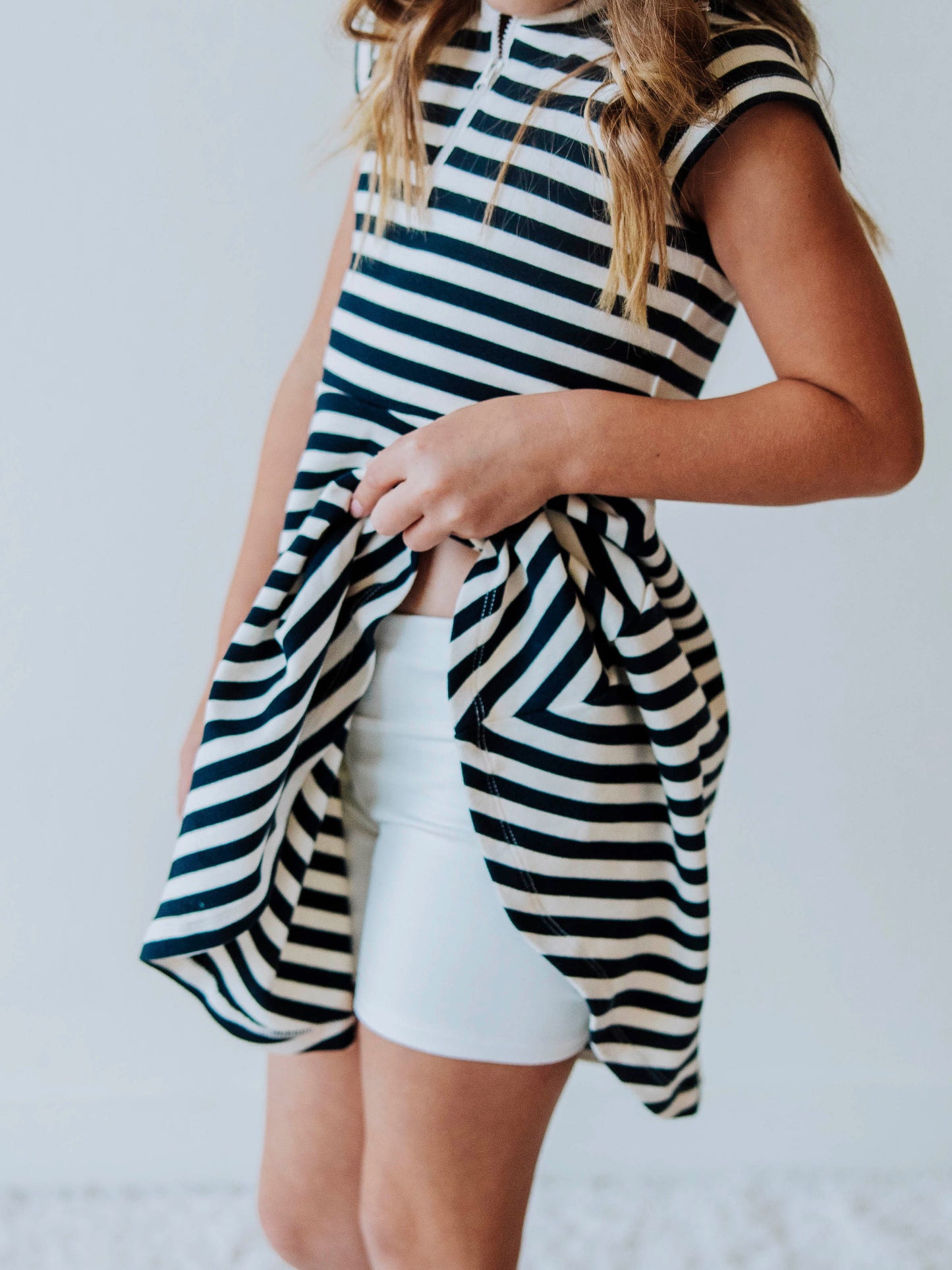 Model is wearing a navy and ivory striped dress and is pulling up the side to show an ivory pair of gym shorts. 