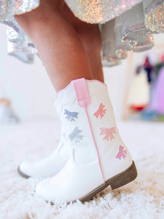Step into sweetness with our Girls Bow Paneled Cowboy Boots, designed for twirls, giggles, and all-day play. These white faux-leather boots feature pastel pink, blue, and lavender star embroidery, charming bow panels, and an easy side zipper closure for quick on-and-off. With a soft interior lining and sturdy sole, these girls’ Western boots perfectly blend comfort and style—ideal for everyday wear, special occasions, or matching with her favorite SweetHoney dress.