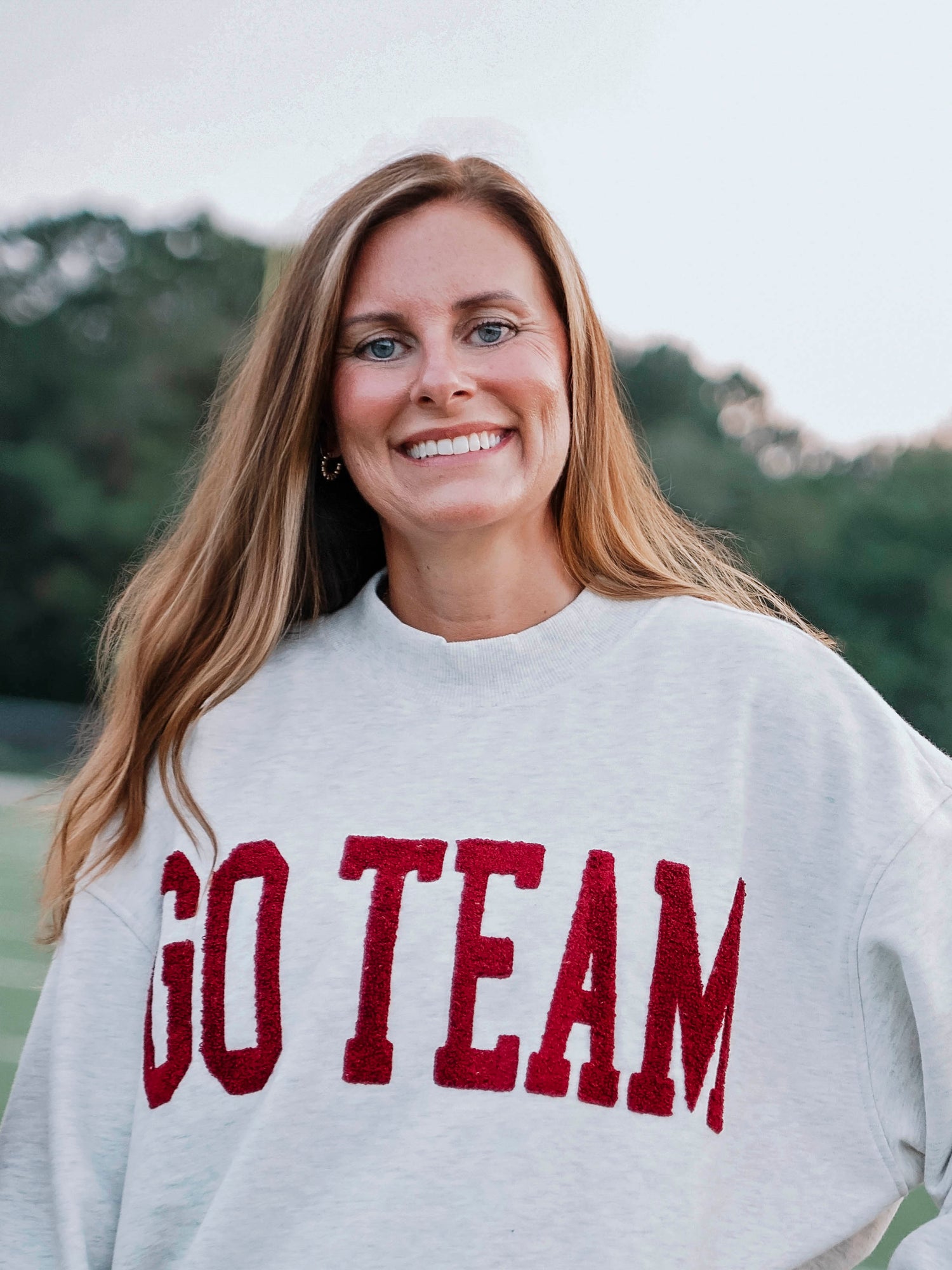 Women outside wearing a heathered gray sweater that says GO TEAM in a crimson red color. 
