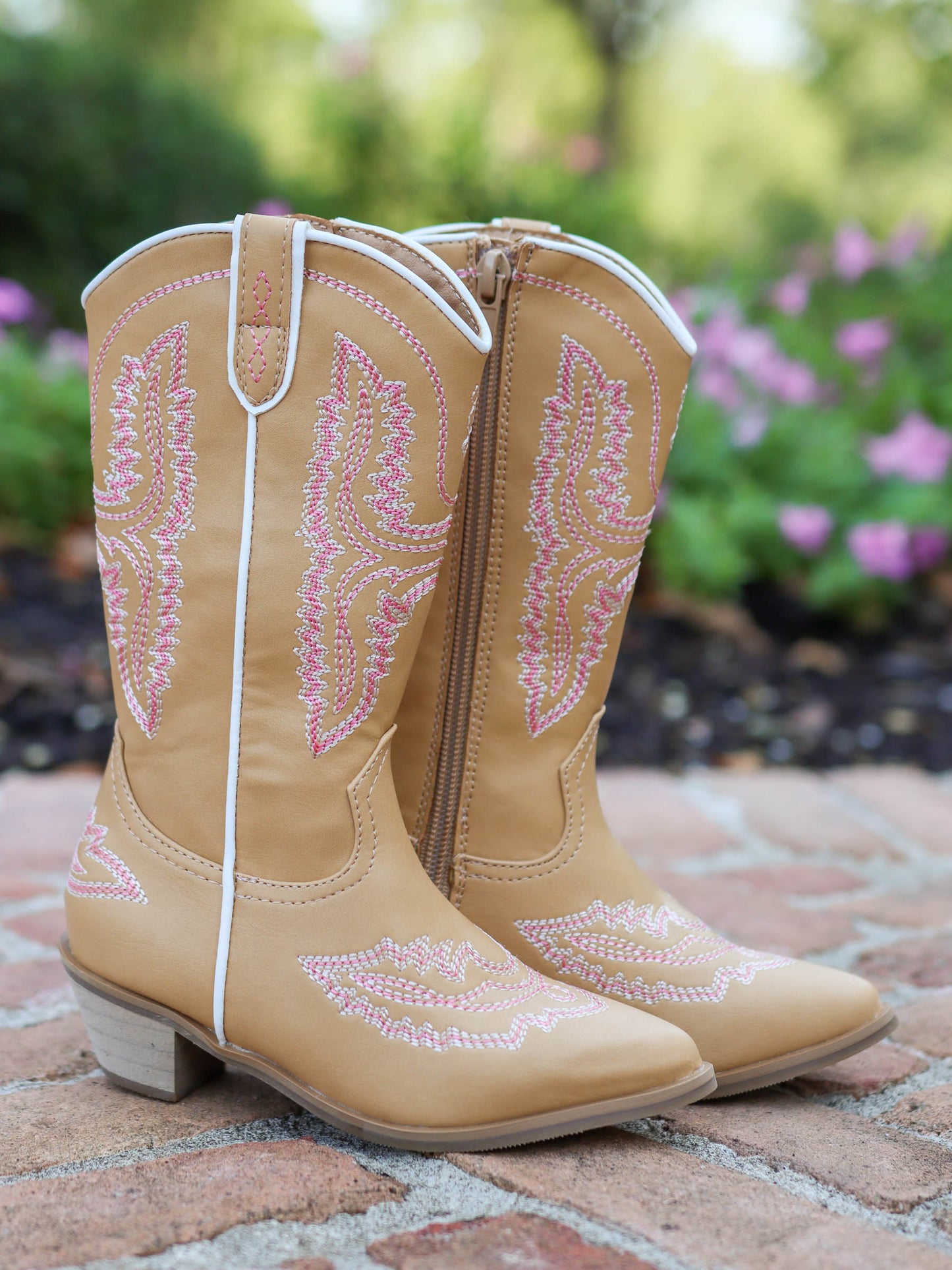Pair of tan, tall, pointy toed boots with pink decorative stitching all over. 