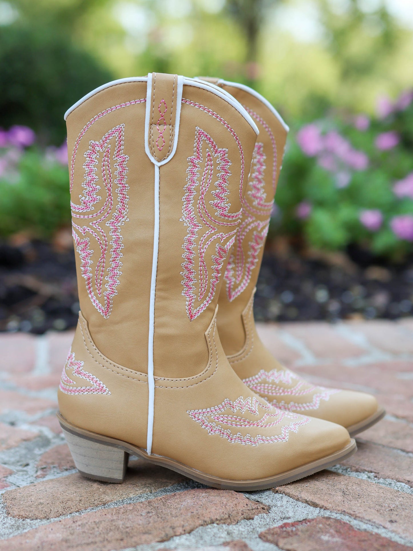 Pair of tan, tall, pointy toed boots with pink decorative stitching all over. 