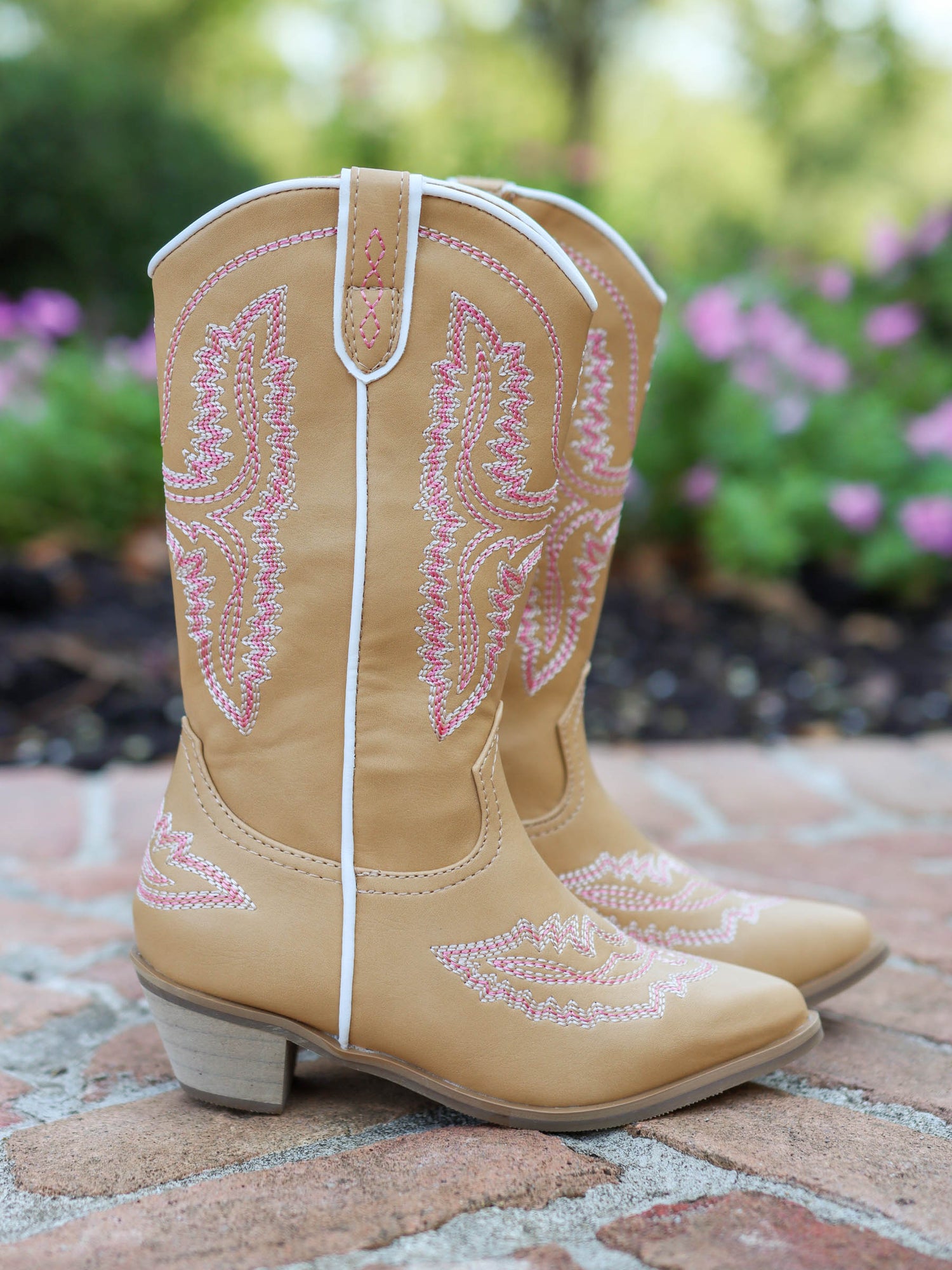 Pair of tan, tall, pointy toed boots with pink decorative stitching all over. 