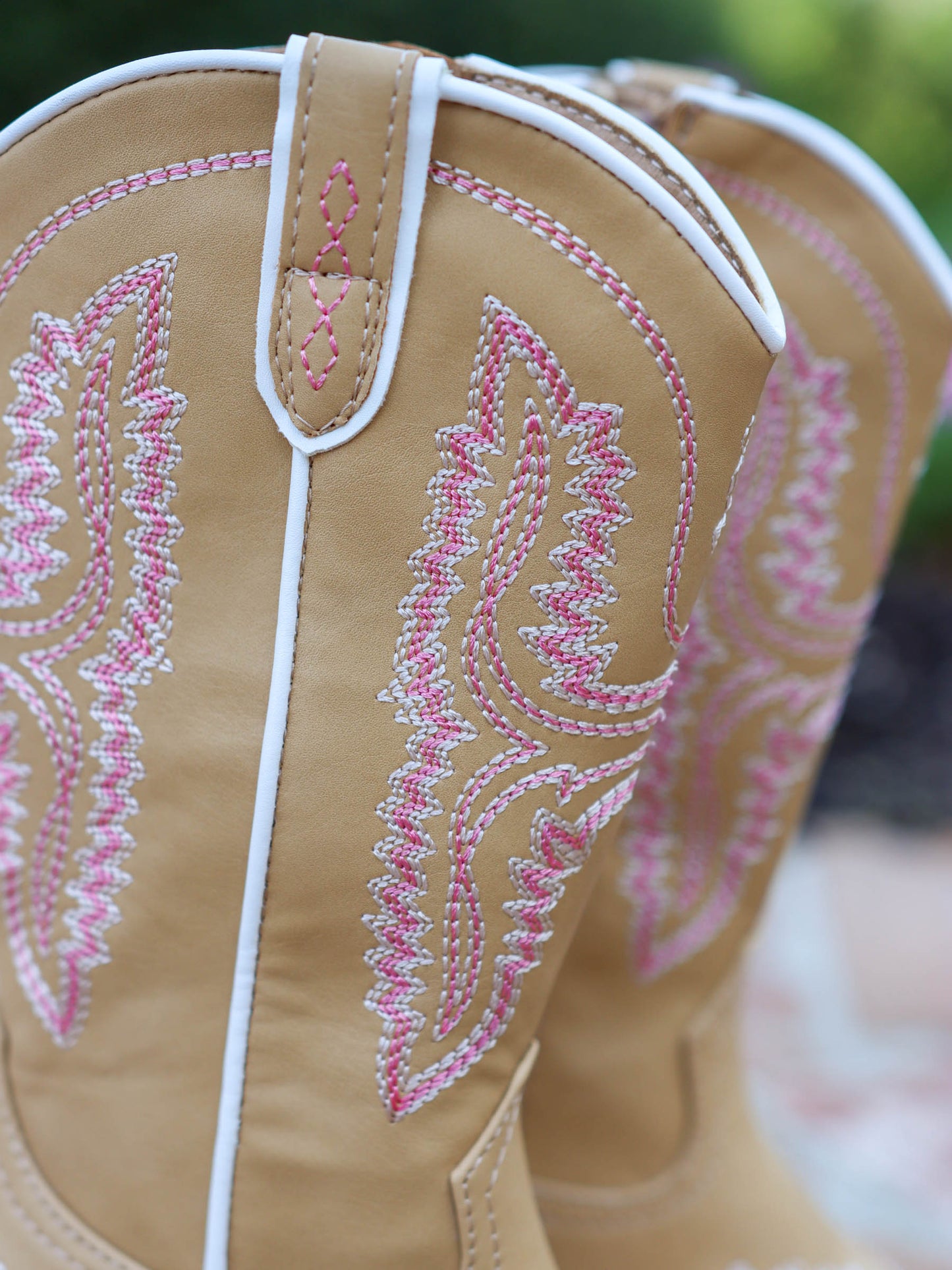 Pair of tan, tall, pointy toed boots with pink decorative stitching all over. this picture shows in detail the pink stitching. 