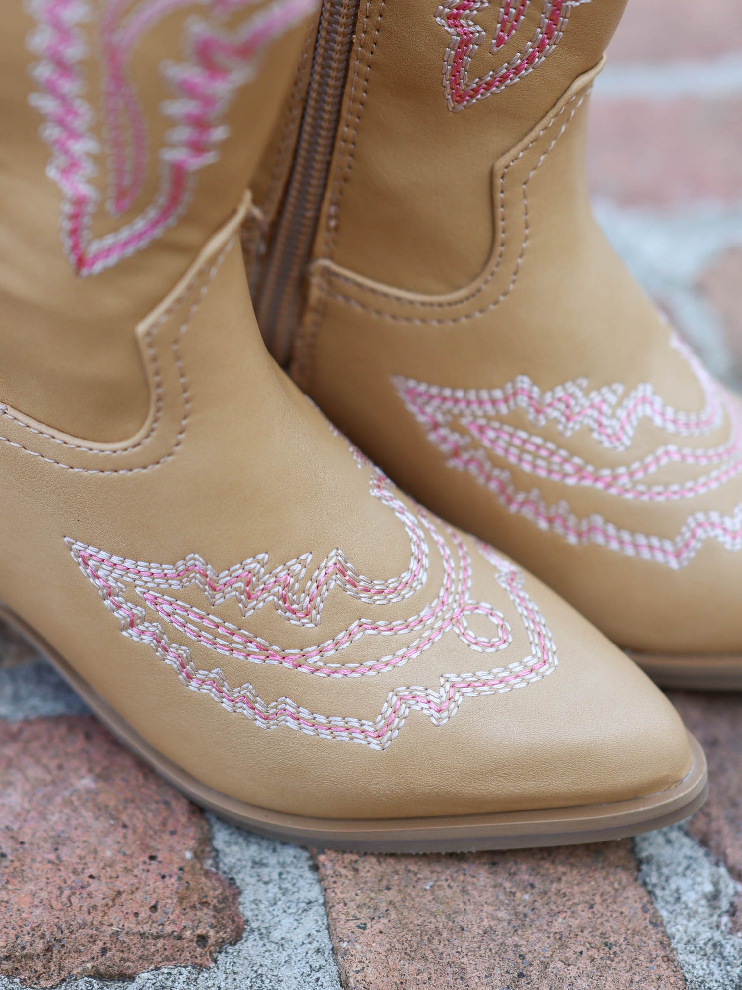 Pair of tan, tall, pointy toed boots with pink decorative stitching all over. This is an up close shot of pointy toe as well as the pink stitching design.