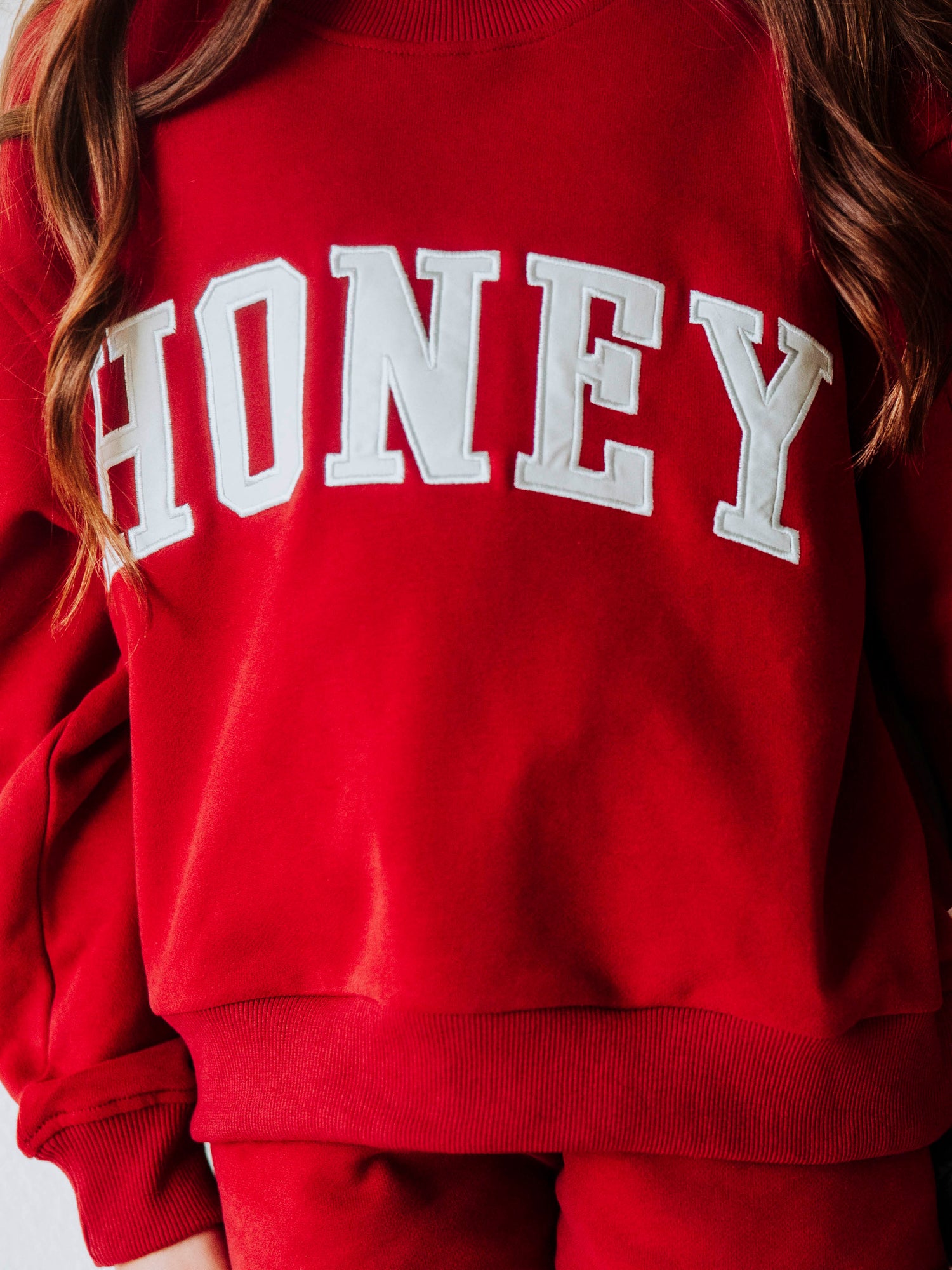 Model is wearing a two-piece, crimson colored, mock net set. The top has HONEY on the front in white letters and the bottoms are the same cromson color as top. Picture is an up close view of top