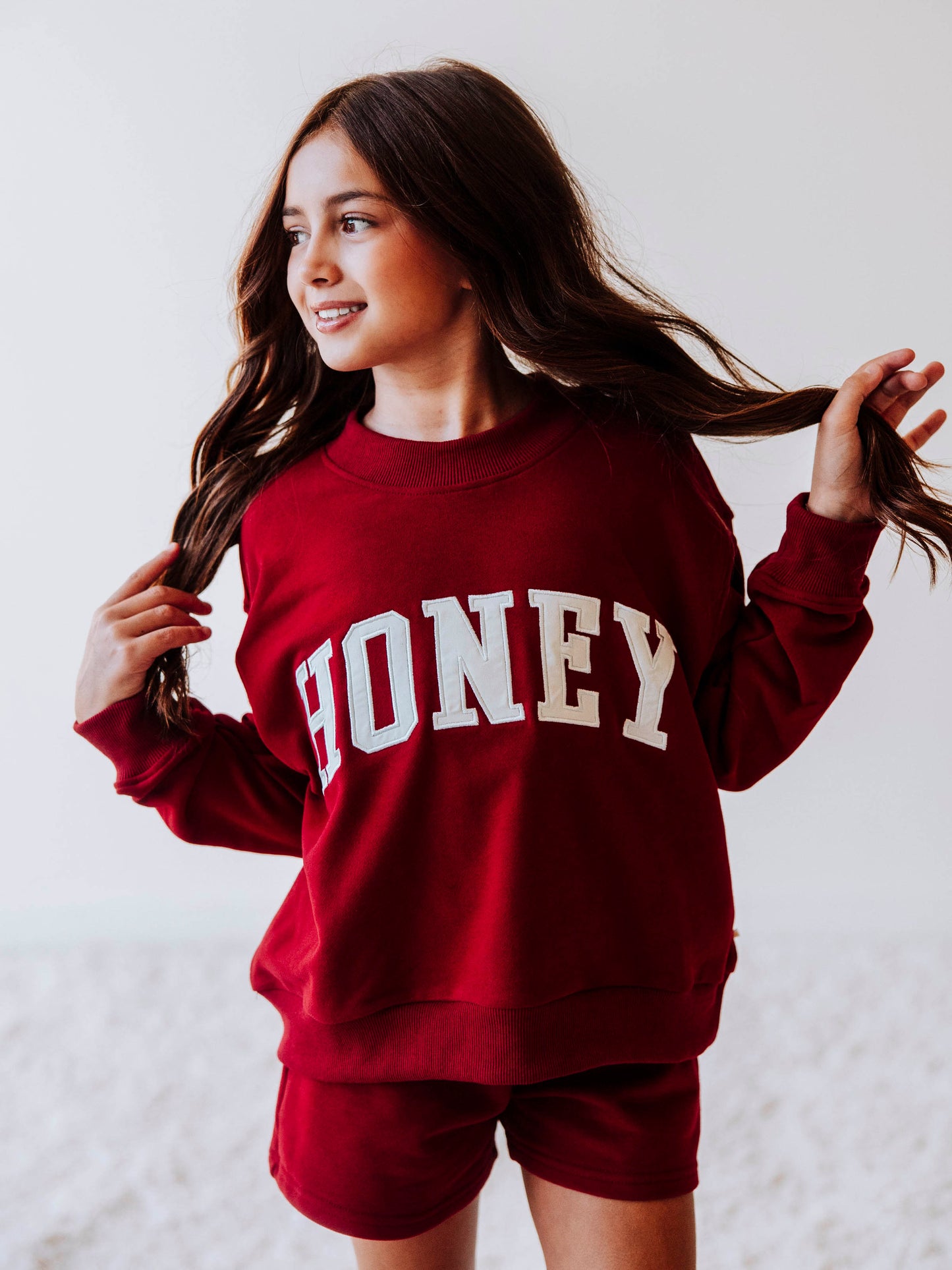 Model is wearing a two-piece, crimson colored, mock net set. The top has HONEY on the front in white letters and the bottoms are the same cromson color as top. 