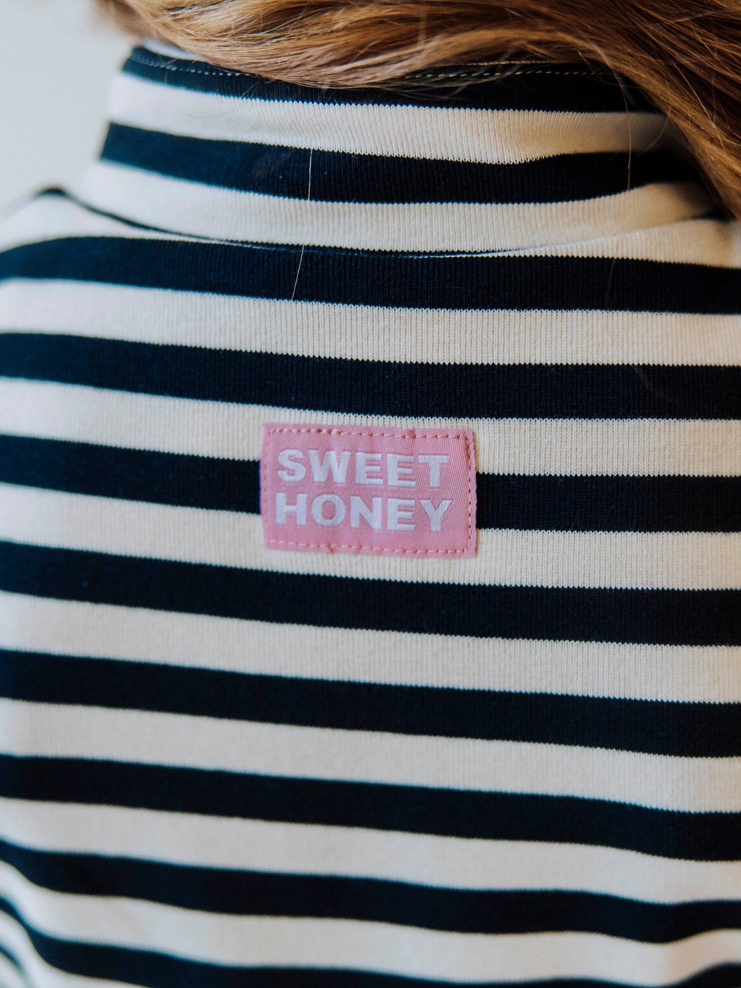 Pink and white stitched SweetHoney logo tag at back of navy and ivory striped dress. 