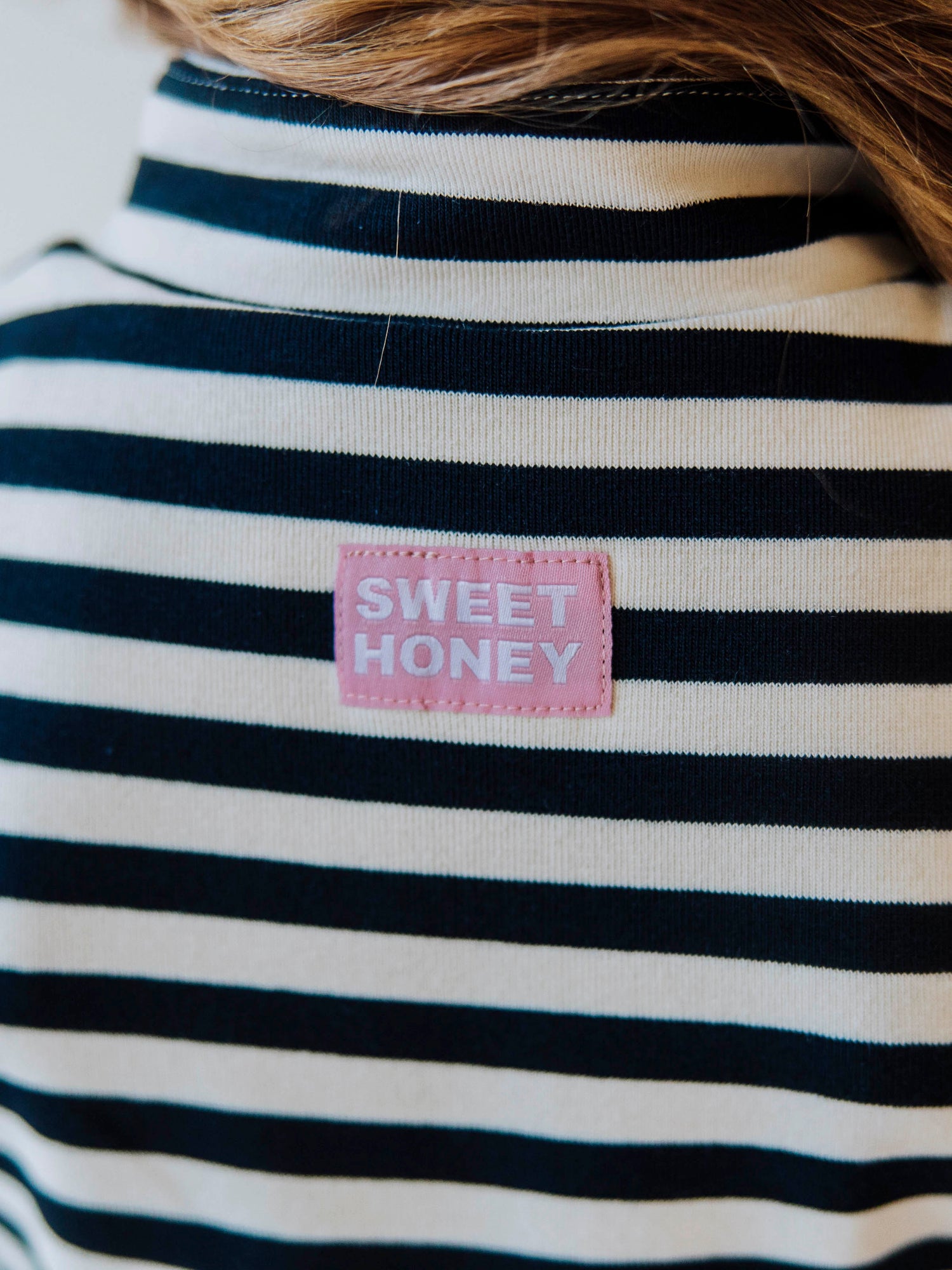 Pink and white stitched SweetHoney logo tag at back of navy and ivory striped dress. 