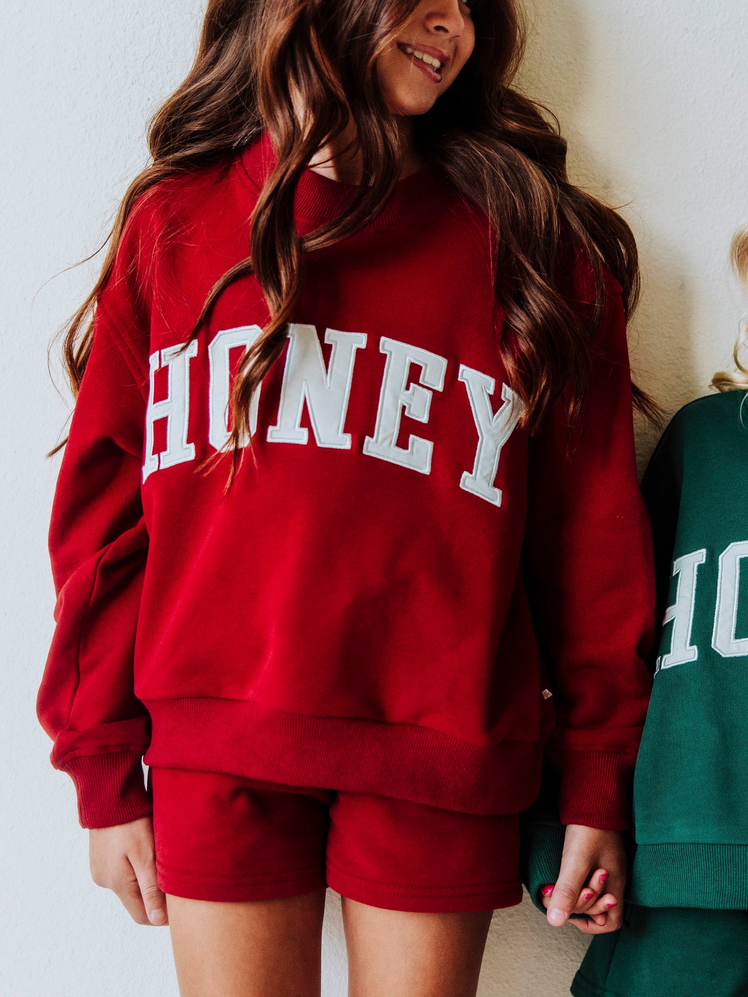 Model is wearing a two-piece, crimson colored, mock net set. The top has HONEY on the front in white letters and the bottoms are the same cromson color as top. 