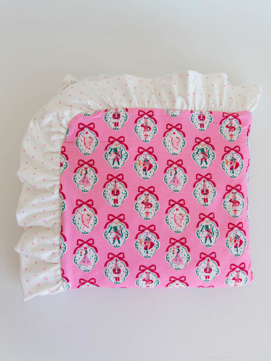 Folded up flay lay of ruffled pink nutcracker printed blanet. 