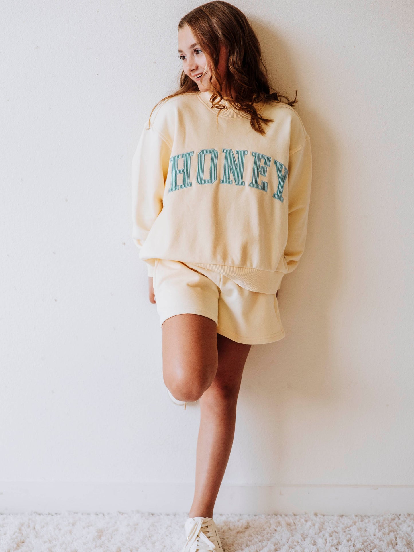 Model wearing a yellow, two-piece mock neck set. The top has HONEY on the front with blue pin stripes. Bottoms are the same color as the top. 