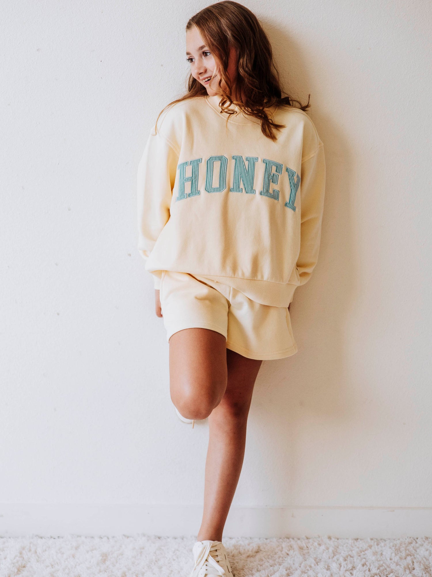 Model wearing a yellow, two-piece mock neck set. The top has HONEY on the front with blue pin stripes. Bottoms are the same color as the top. 