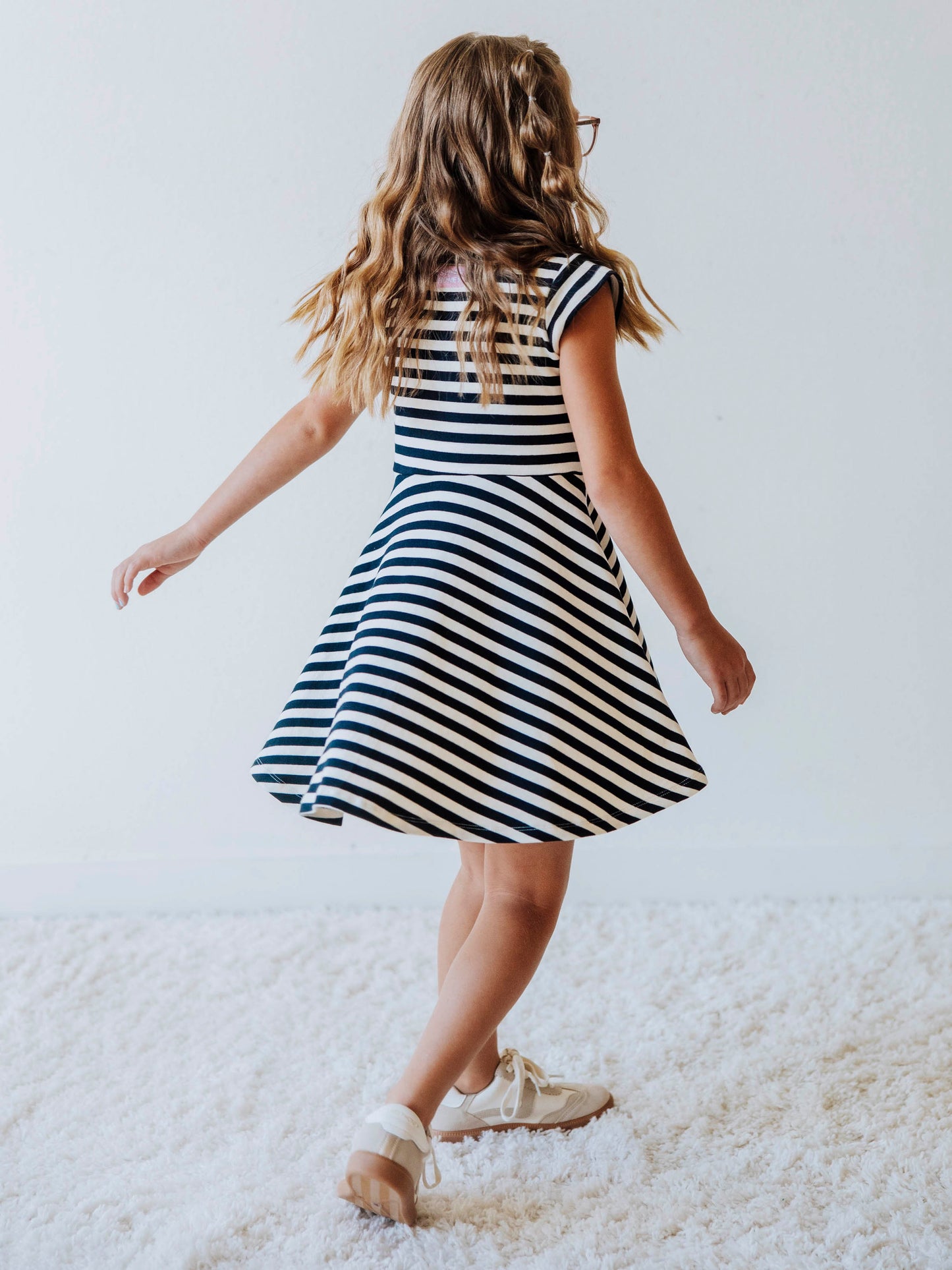 Model is wearing a navy and ivory striped dress with cream colored shoes. Model is twirling. 