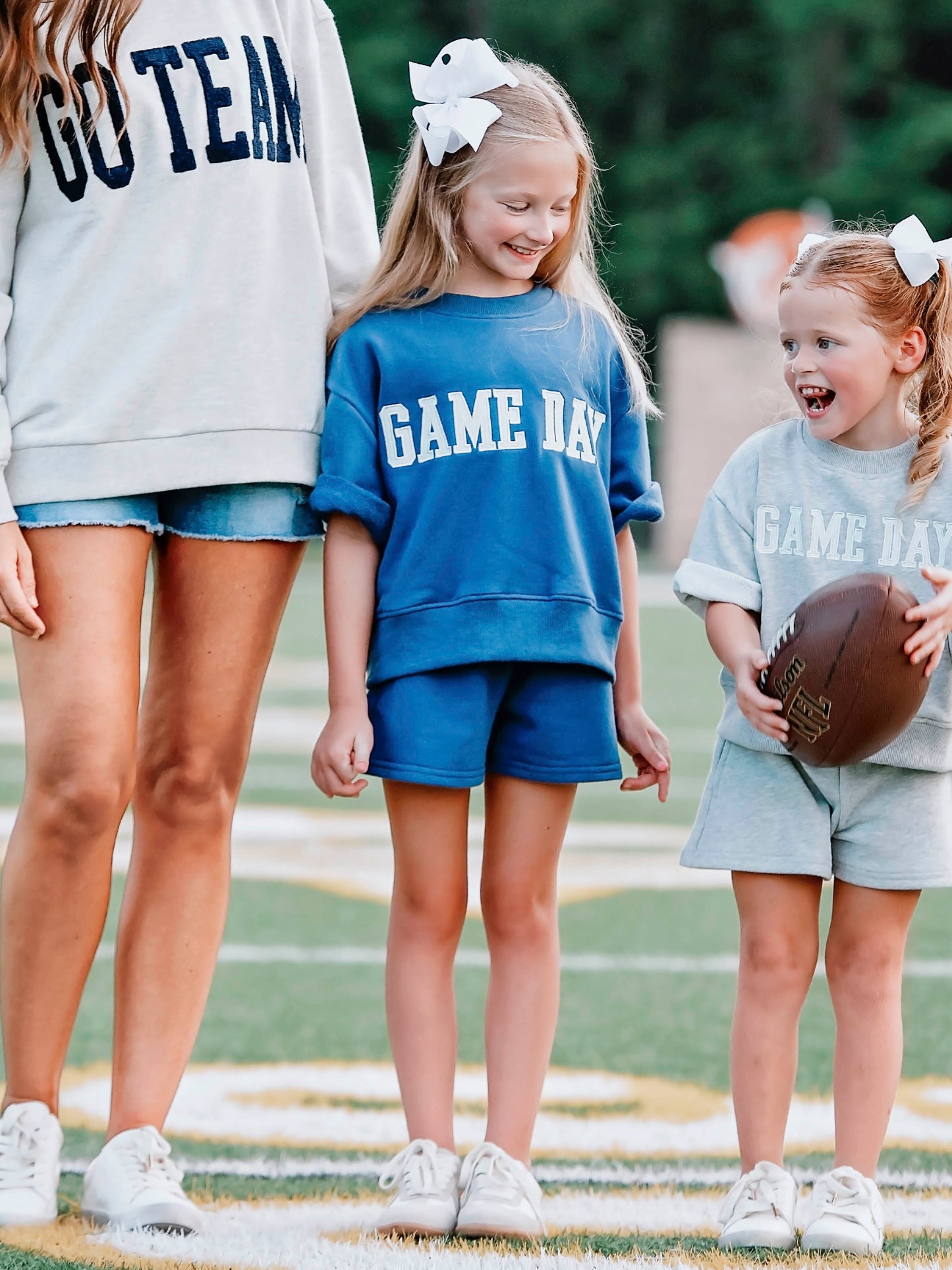 Girl outside wearing a two piece navy set that says GAME DAY on the front. Girl is standing next to another child and an adult